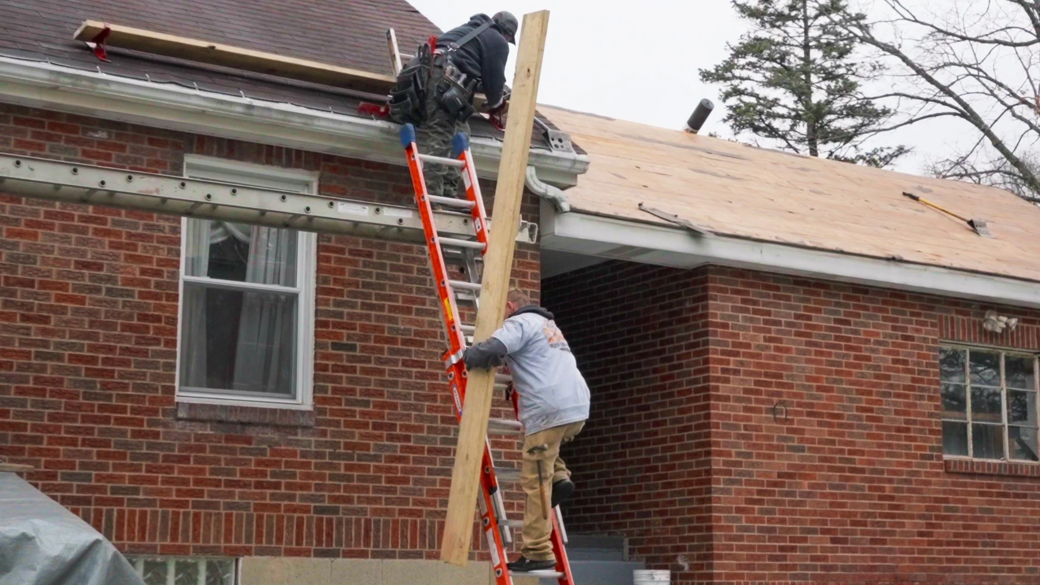 Pittsburgh roofers working outdoors, one with a white hoodie with a business logo and the other with a red hoodie, working on a roof repair project.