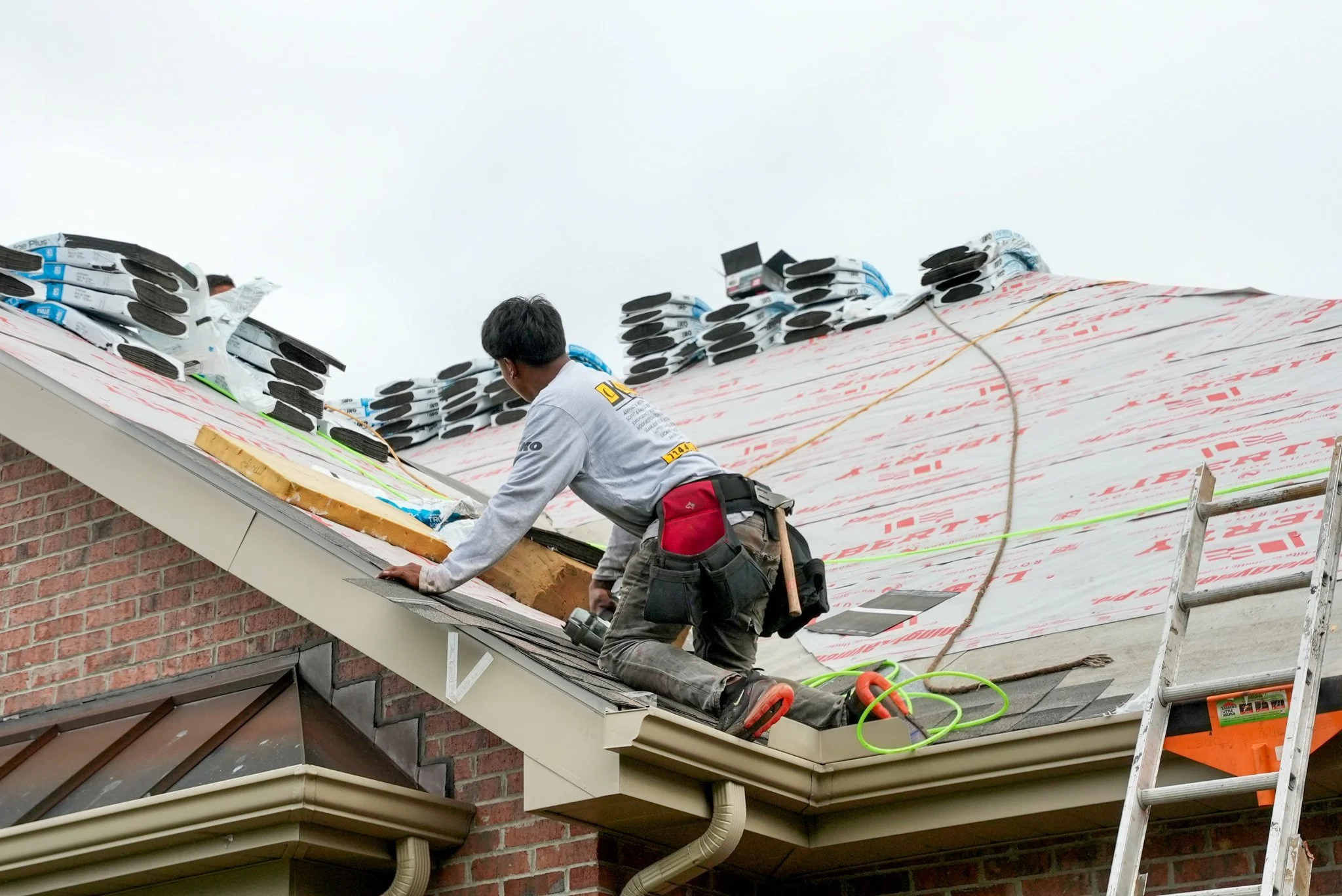 A Pittsburgh construction worker installing or repairing a roof on a brick house, with roofing materials and tools nearby.