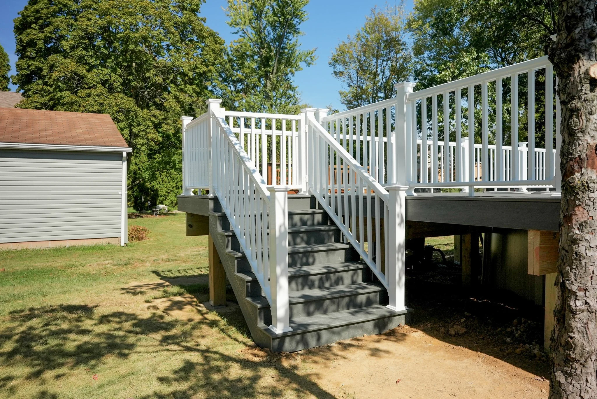 Newly built white wooden staircase with railings leading up to a deck in a backyard with green grass and trees.