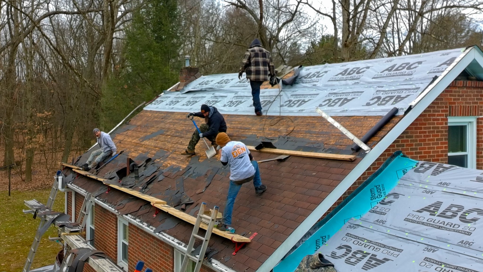 Pittsburgh roofers working outdoors, one with a white hoodie with a business logo and the other with a red hoodie, working on a roof repair project.
