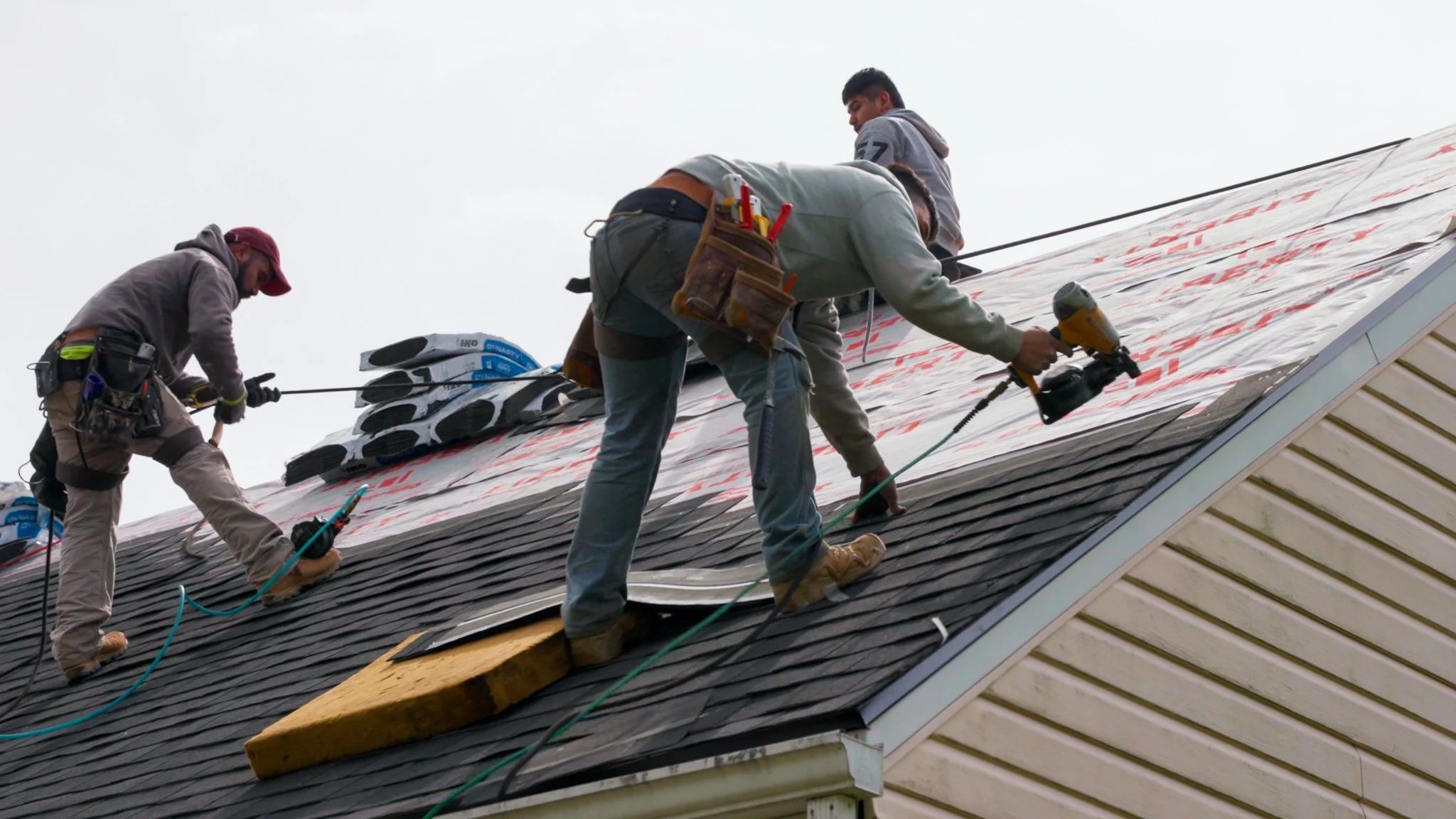 Pittsburgh roofers working outdoors, one with a white hoodie with a business logo and the other with a red hoodie, working on a roof repair project.