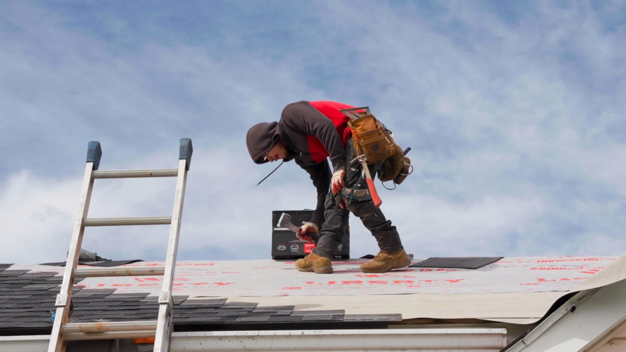 Pittsburgh roofers working outdoors, one with a white hoodie with a business logo and the other with a red hoodie, working on a roof repair project.
