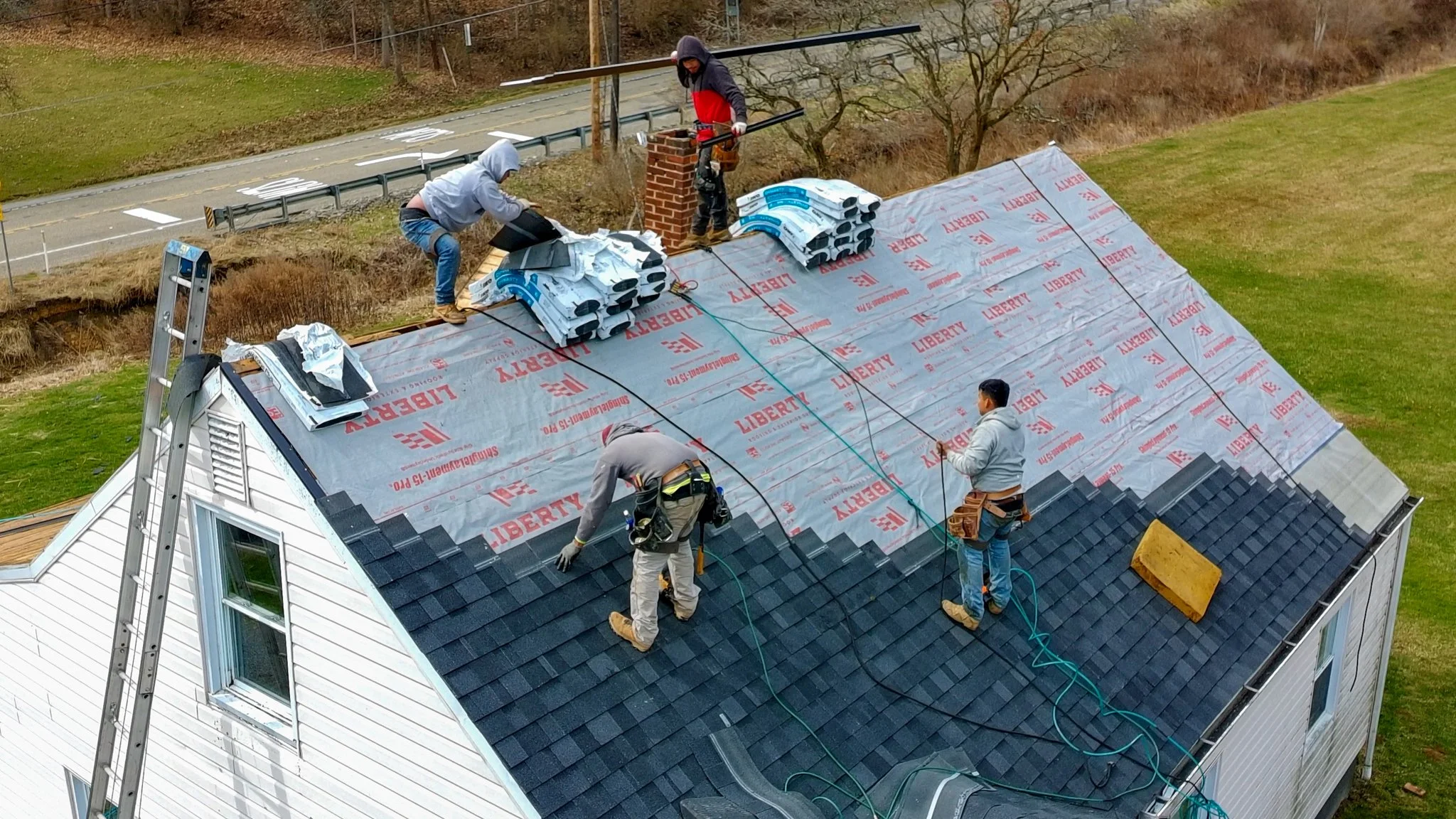 Two Pittsburgh roofers working outdoors, one with a white hoodie with a business logo and the other with a red hoodie, working on a roof repair project.