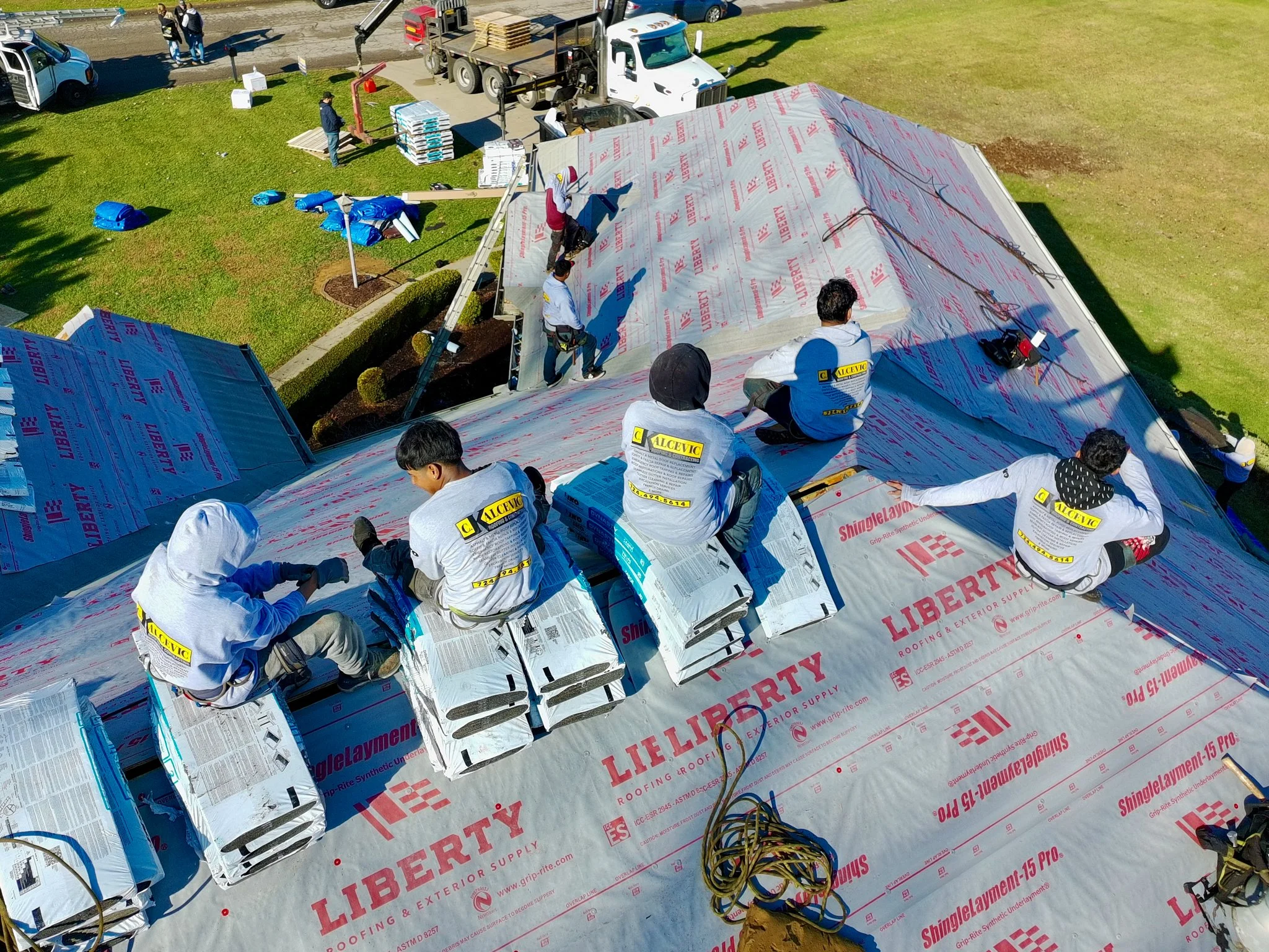 Pittsburgh workers installing shingle roofing on a building, with various construction tools and materials around them.