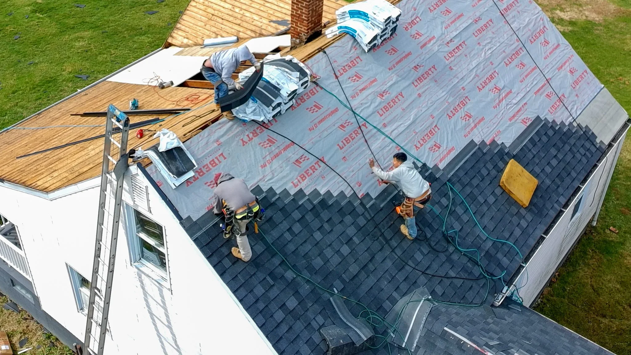 Two Pittsburgh roofers working outdoors, one with a white hoodie with a business logo and the other with a red hoodie, working on a roof repair project.