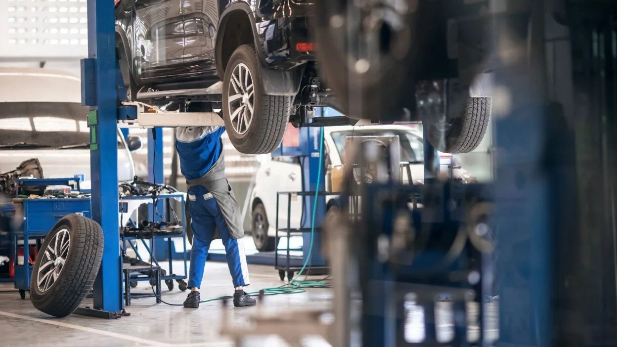 Mechanic inspecting a car on a hydraulic lift inside an auto repair workshop