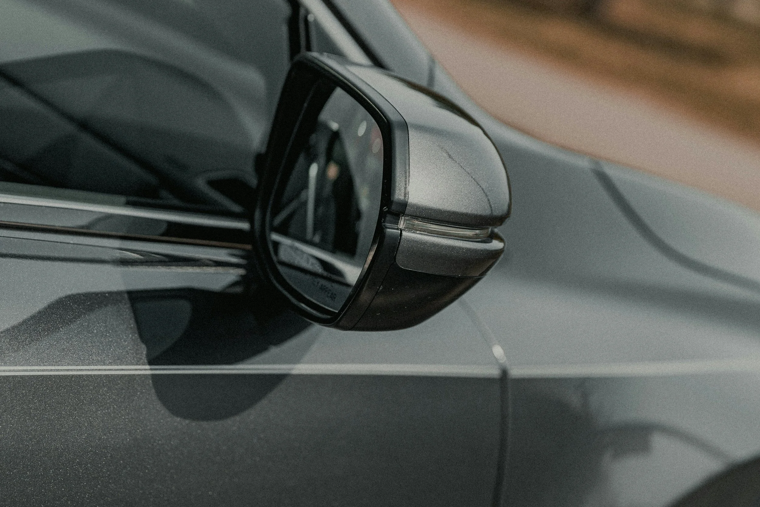 Close-up of a side mirror on a gray car, showing the mirror mounted on the driver side door.