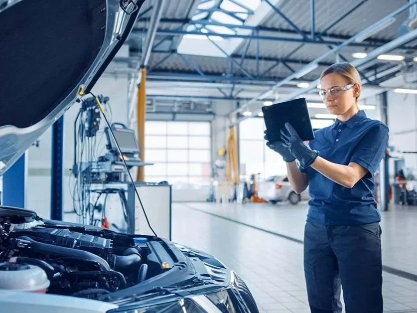 Auto technician using a digital tablet to inspect a vehicle in a modern repair facility, analyzing performance and workflow efficiency