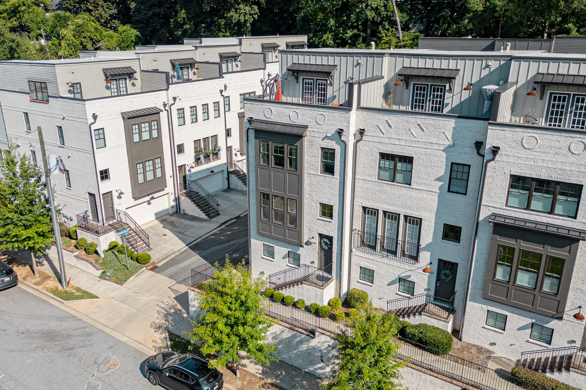 Aerial view of modern white apartment buildings with black and brown accents, small front yards, stairs, and trees lining the sidewalk.