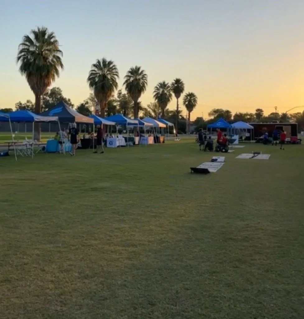 Outdoor event setup in a park with many tents, palm trees, and people during sunset.