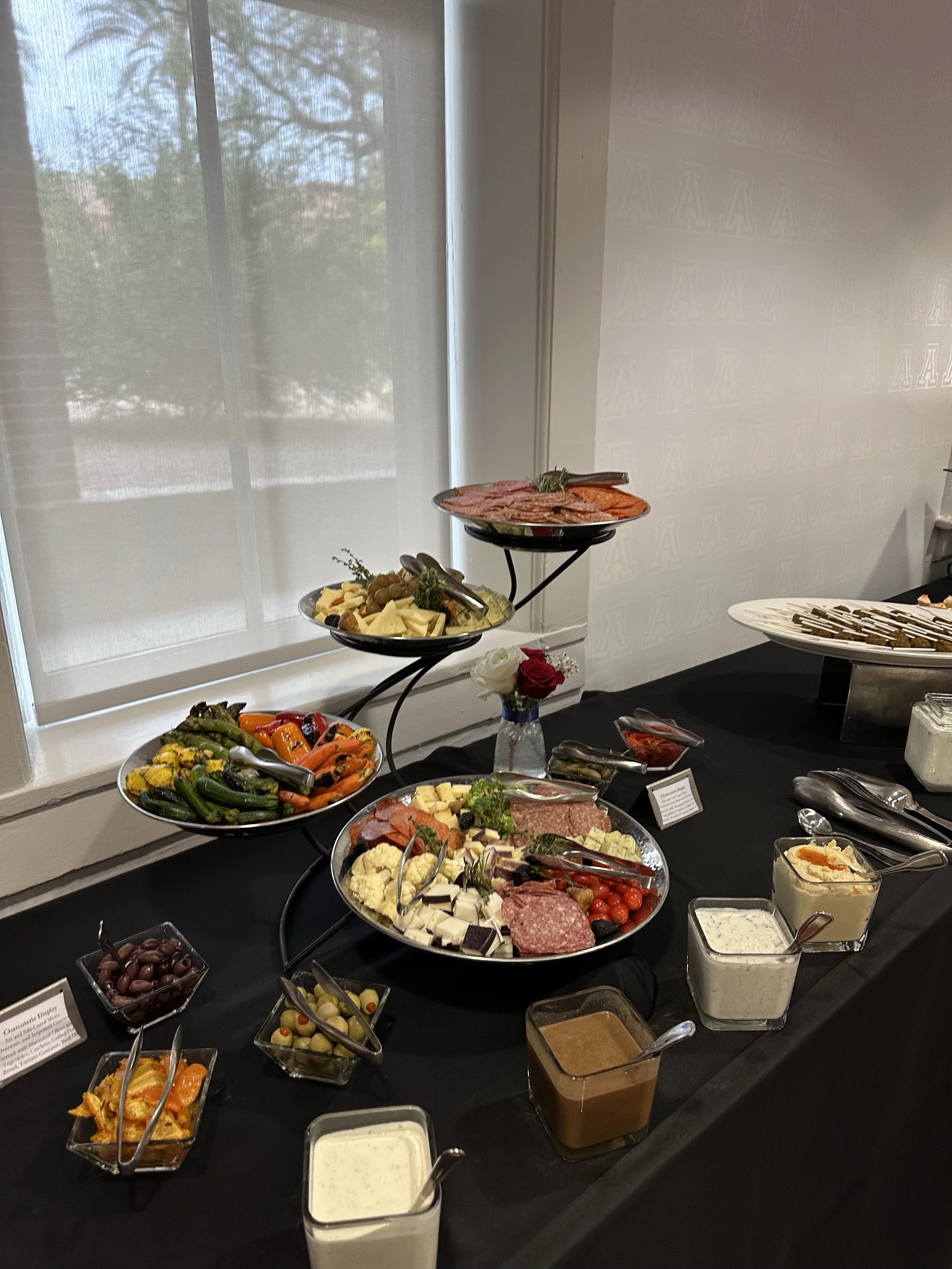 Assorted cheeses, meats, vegetables, and condiments on a buffet table with bowls of olives, sauces, and garnishes.