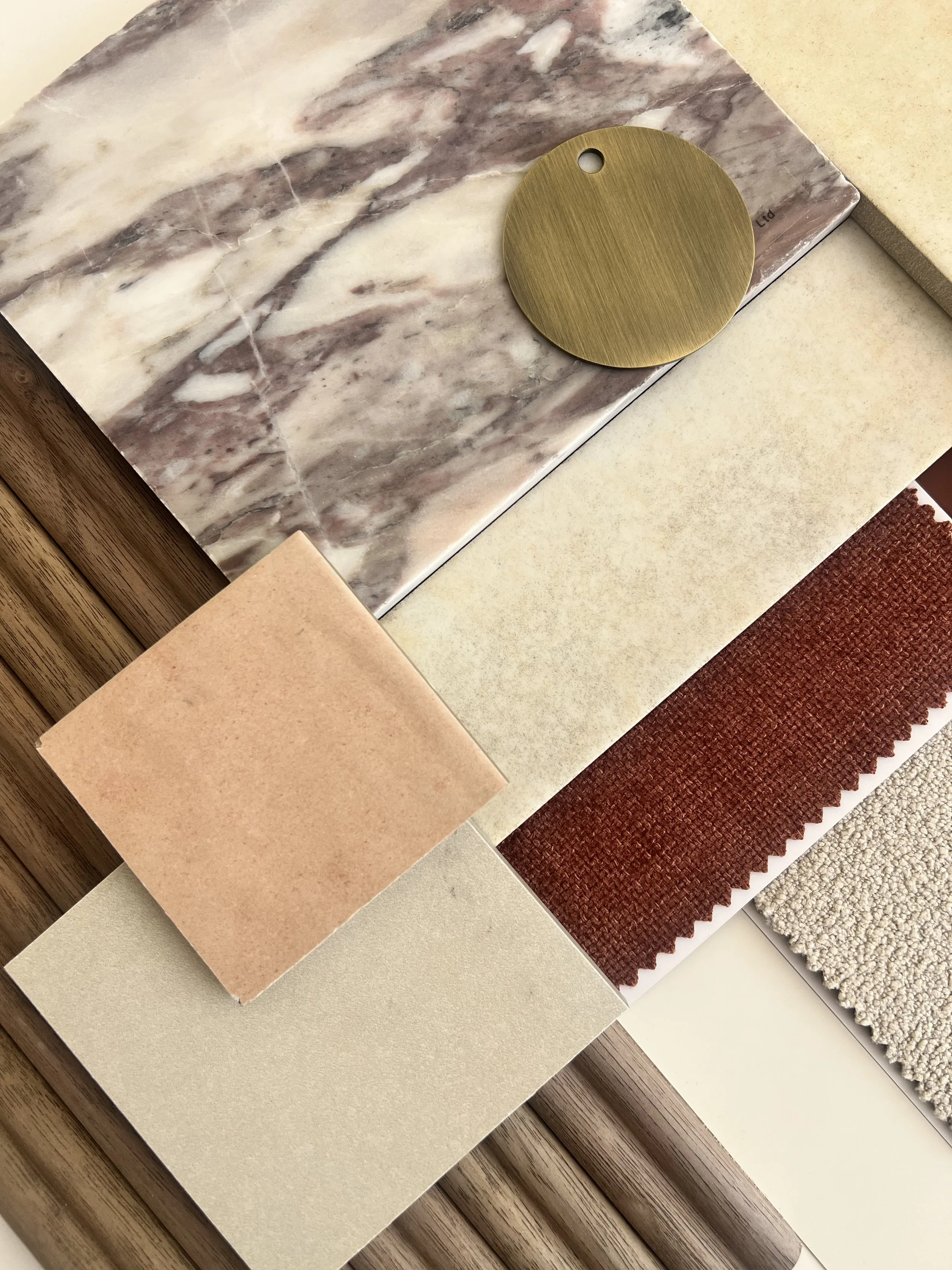 A collection of material samples, including a marble slab, wood textures, fabric swatches in red and beige, and a brass circle, conveys a warm, earthy palette.