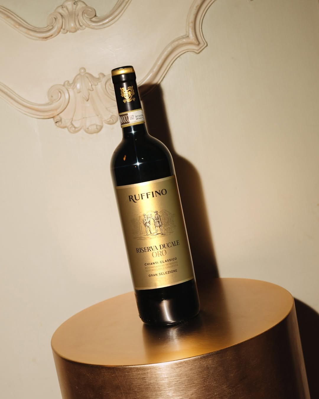 A bottle of Ruffino Riserva Ducale Oro Chianti Classico wine placed on a wooden surface in front of a decorative ceiling detail.