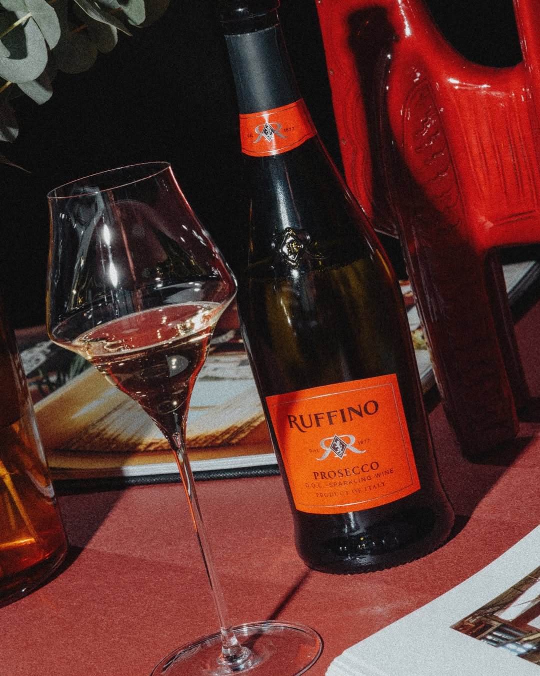 A glass of rosé wine in front of a bottle of Ruffino Prosecco and a red plastic crate on a table at a restaurant.
