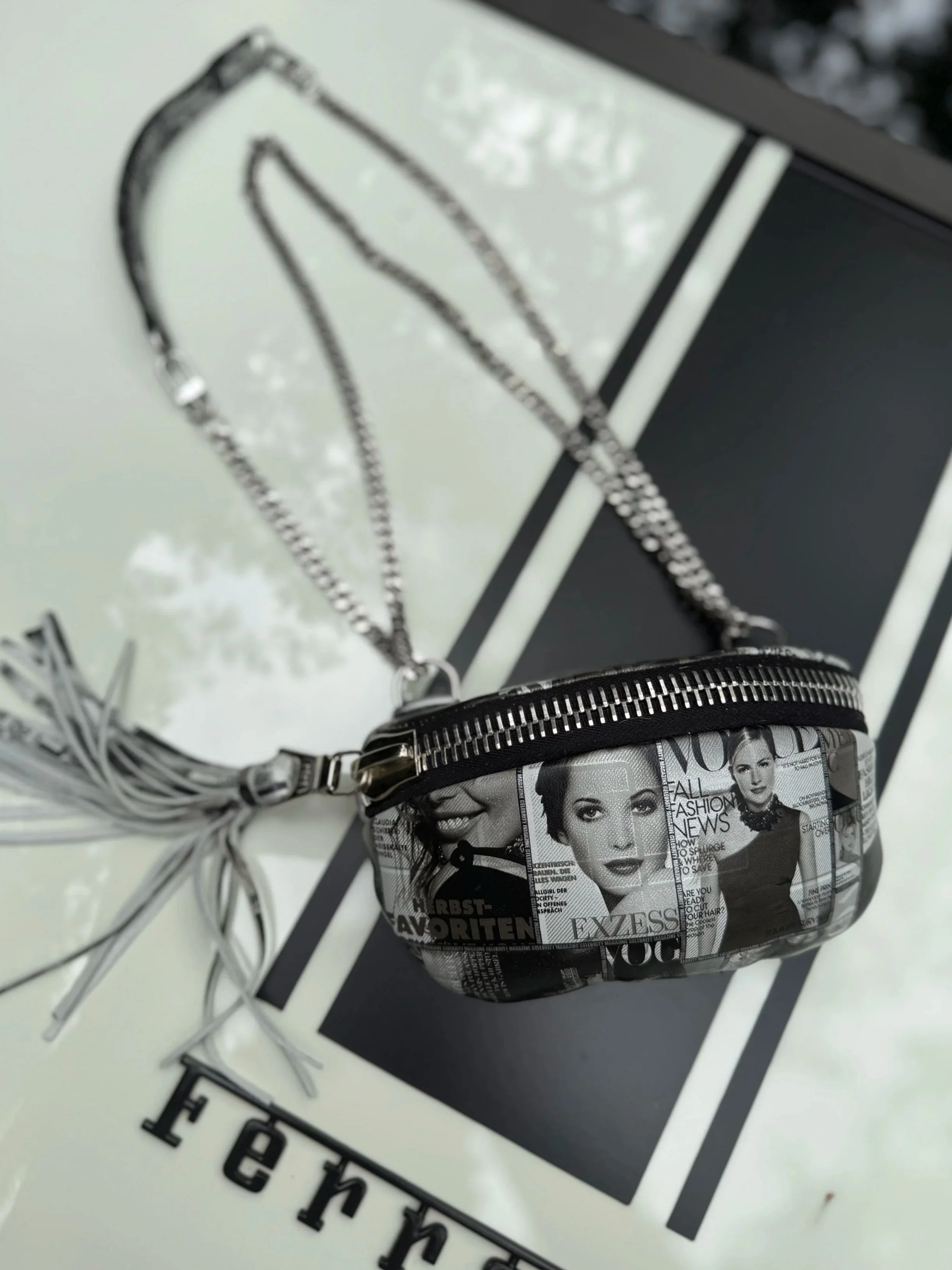 Black and white newspaper-print shoulder bag with a silver chain strap and editorial-inspired details.