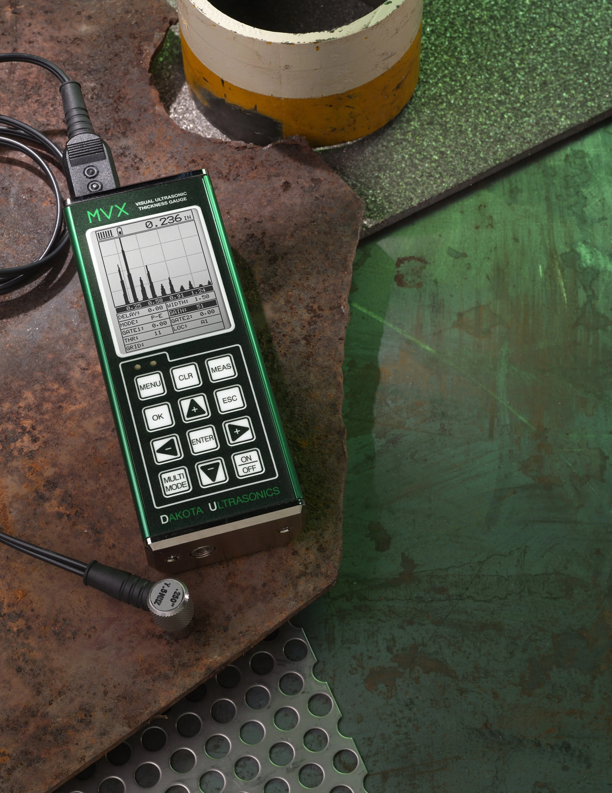 Un medidor de ultrasonidos en una superficie de hierro oxidado, rodeado de algunos objetos de cemento y metal.