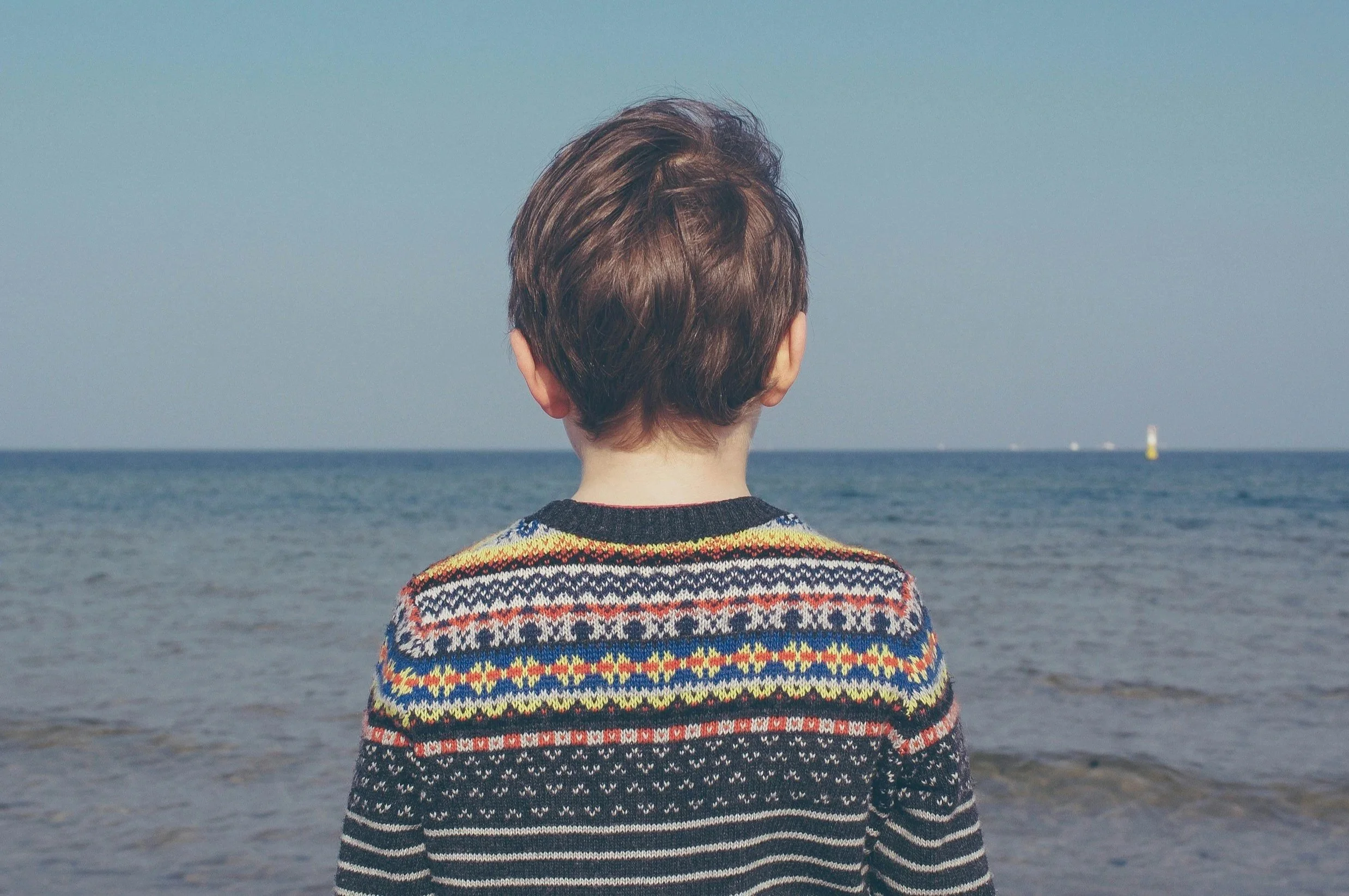 Young boy looking out at the ocean, reflecting on feelings and growth, symbolizing emotional exploration and child therapy support