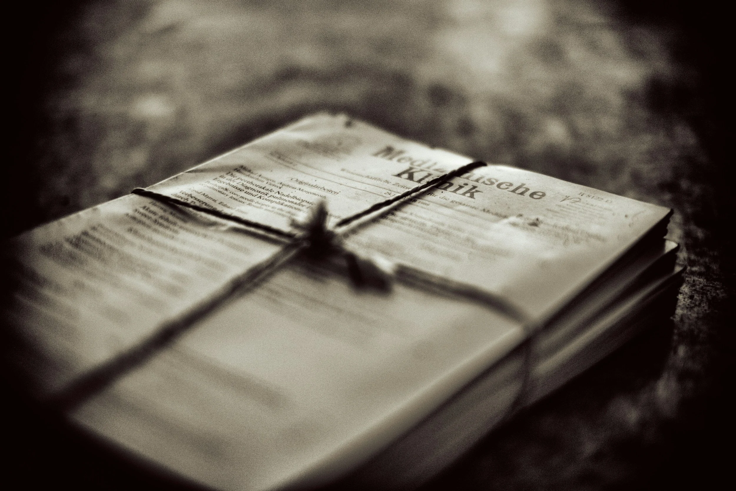 A bundle of old newspapers tied with string, lying on a dark surface, with the visible headline in German.