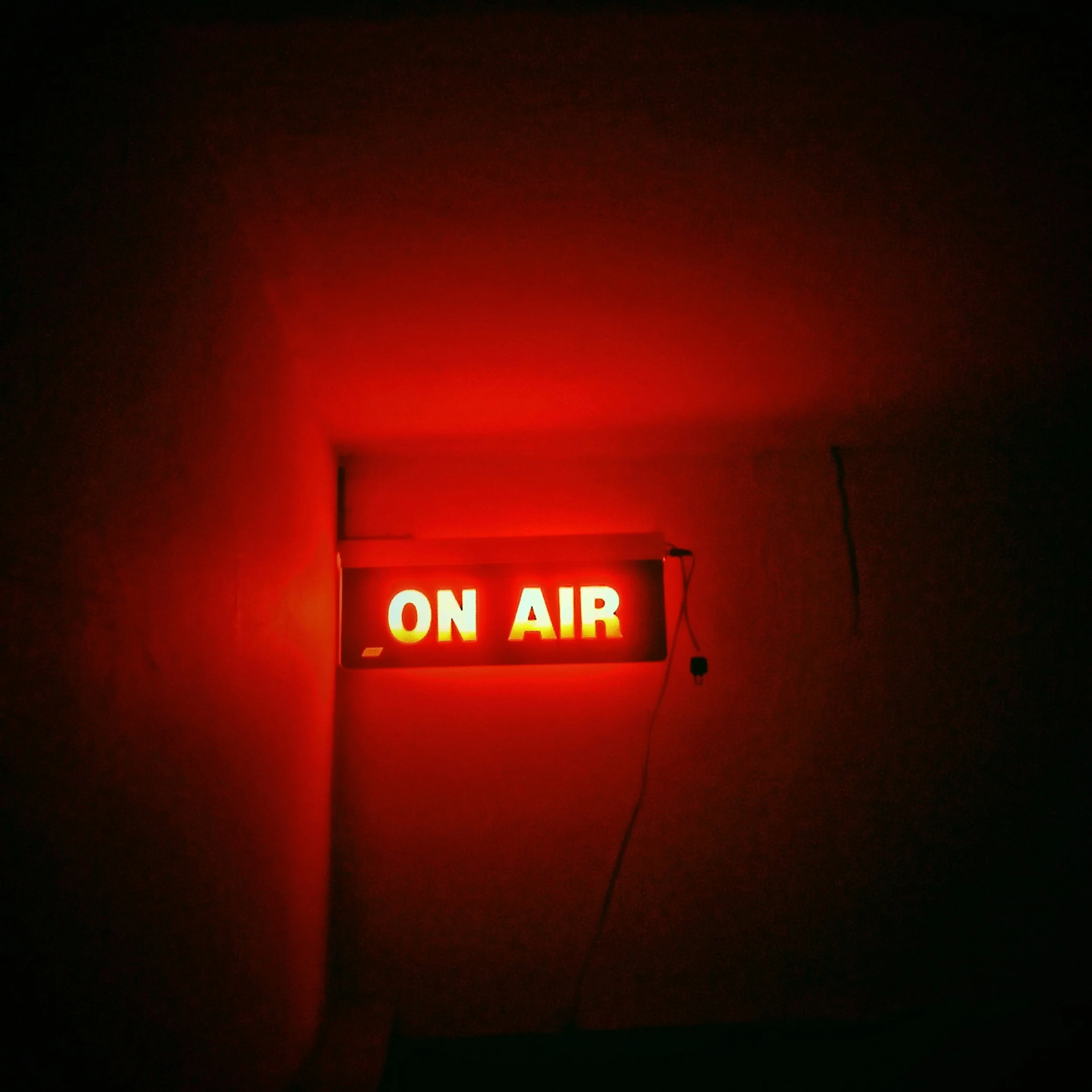 Red illuminated 'ON AIR' sign hanging on the wall in a dark room.