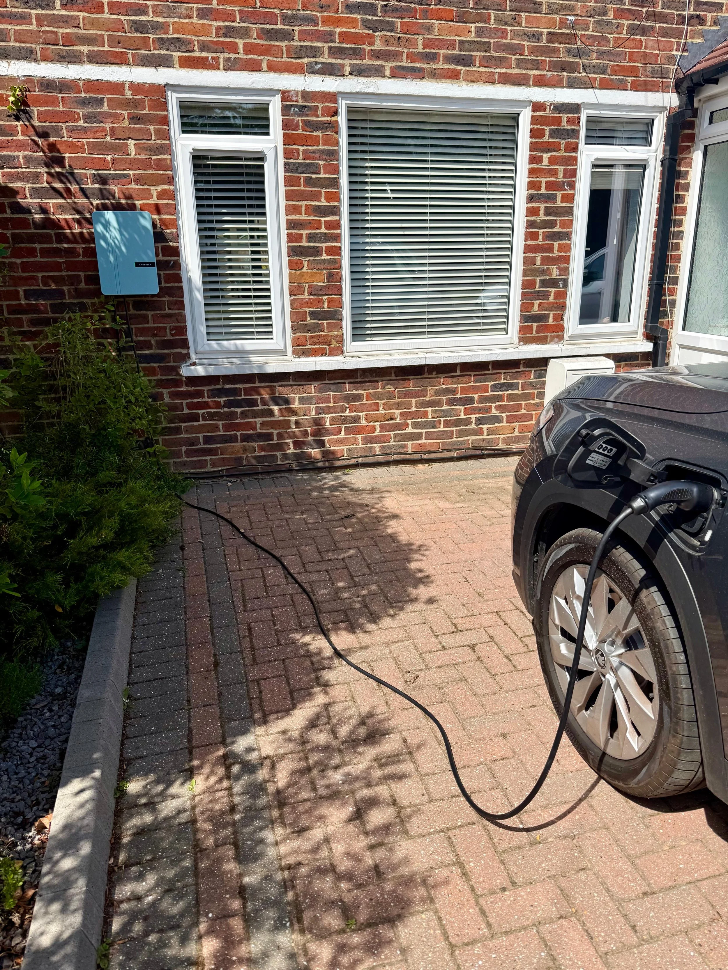 EV charger installation on a brick house, with a car charging on the driveway