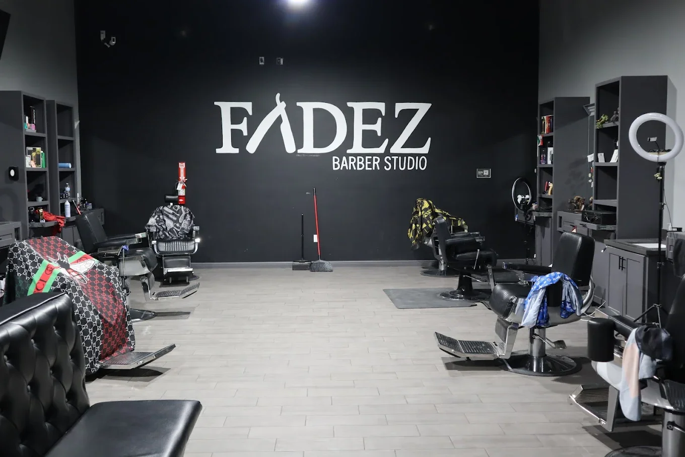 Interior of a barber studio named Fadez with black walls, several barber chairs, shelves with barber supplies, and a large Fadez sign on the back wall.