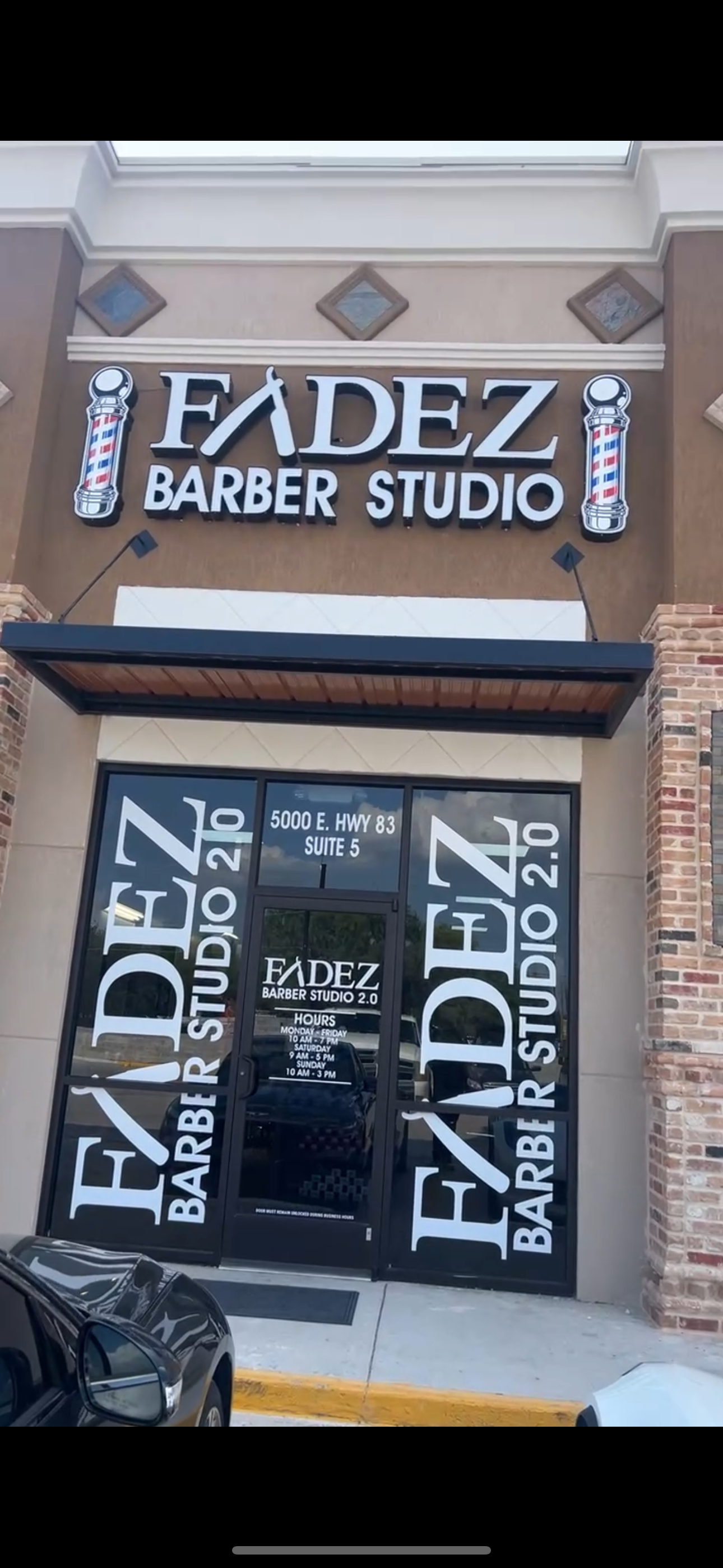 The storefront of Fadez Barber Studio, showing the name and address, with hanging signs and glass doors.