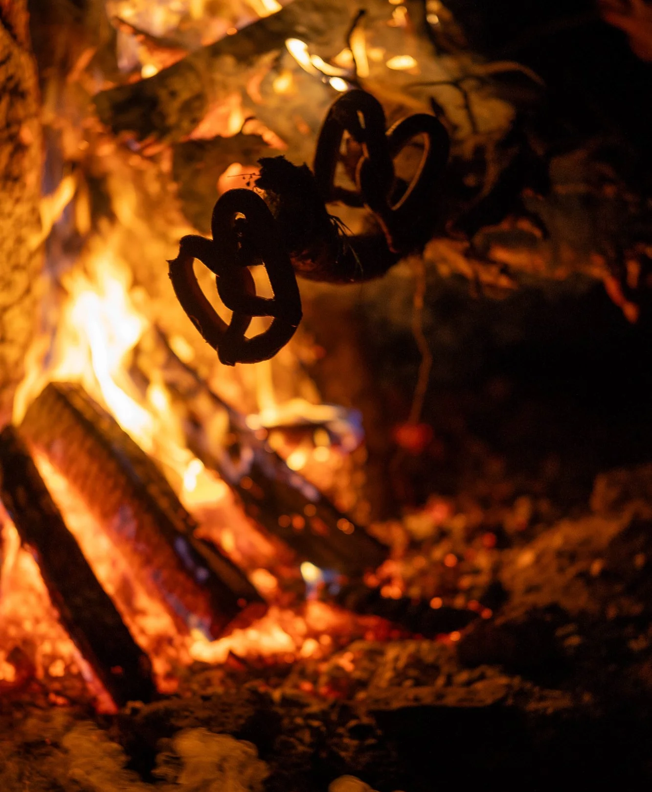 A campfire with soft pretzels hanging above the fire, glowing embers and burning logs.