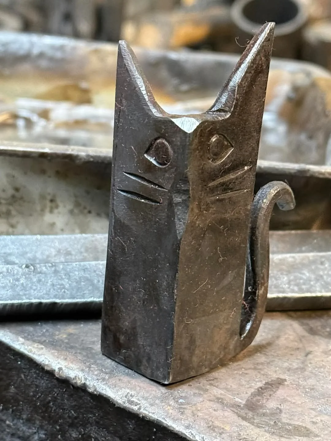 A small metal sculpture of a cat with carved facial features, including eyes, a nose, and a mouth, attached to a metal bar.