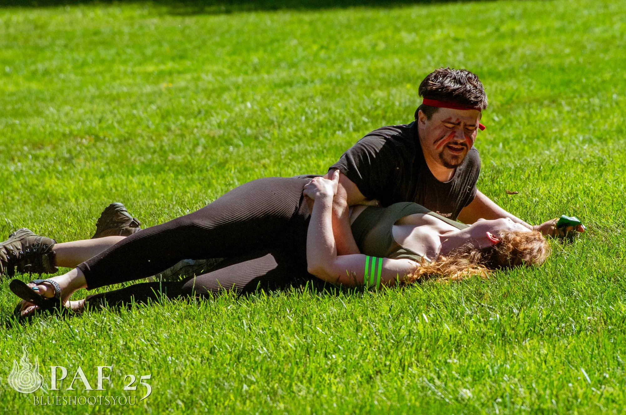 A man and a woman on the grass, with the man pinning the woman down; both playfully wrestling.