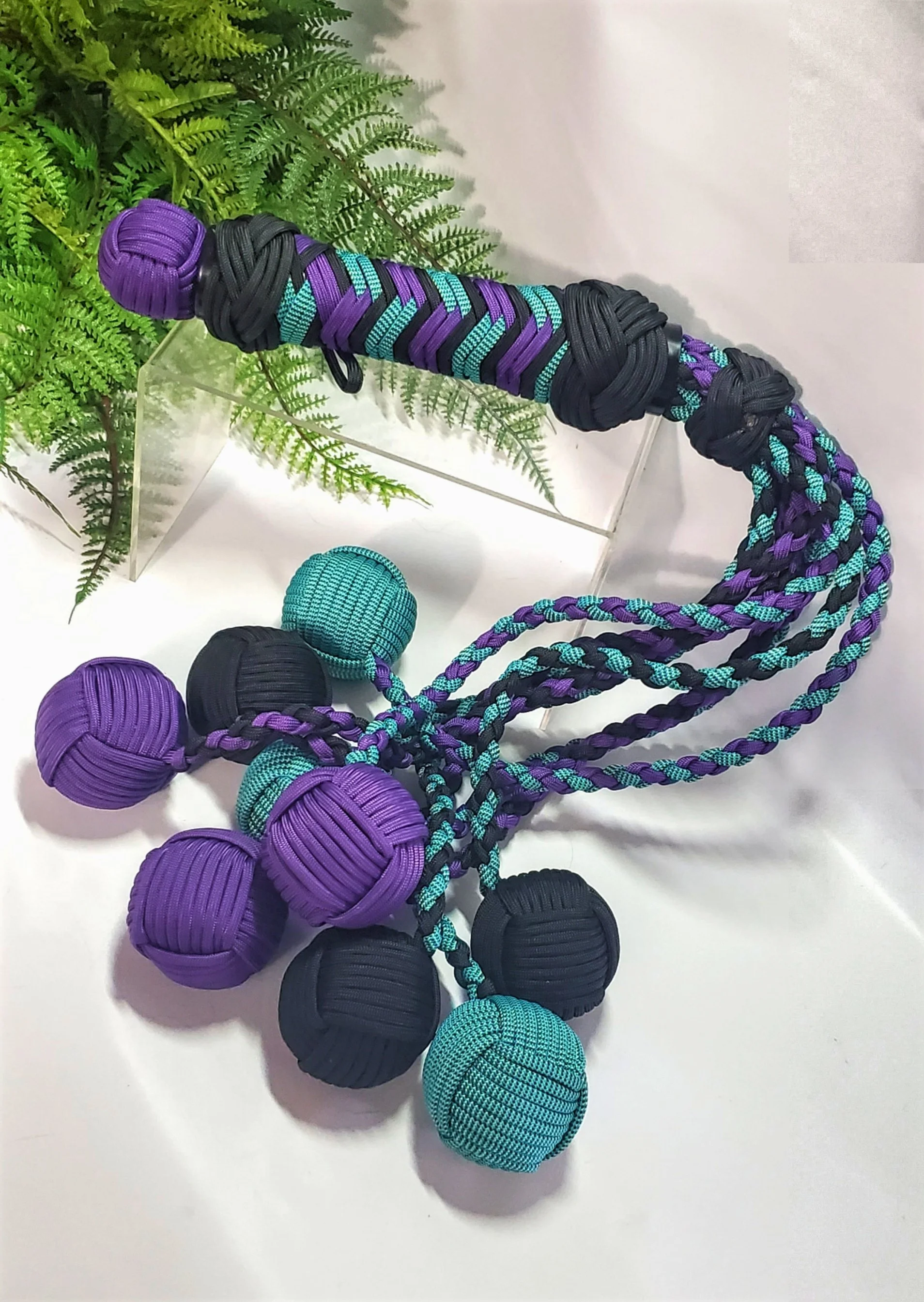 Purple, black, and turquoise impact toy, displayed on a white surface with green fern leaves nearby.