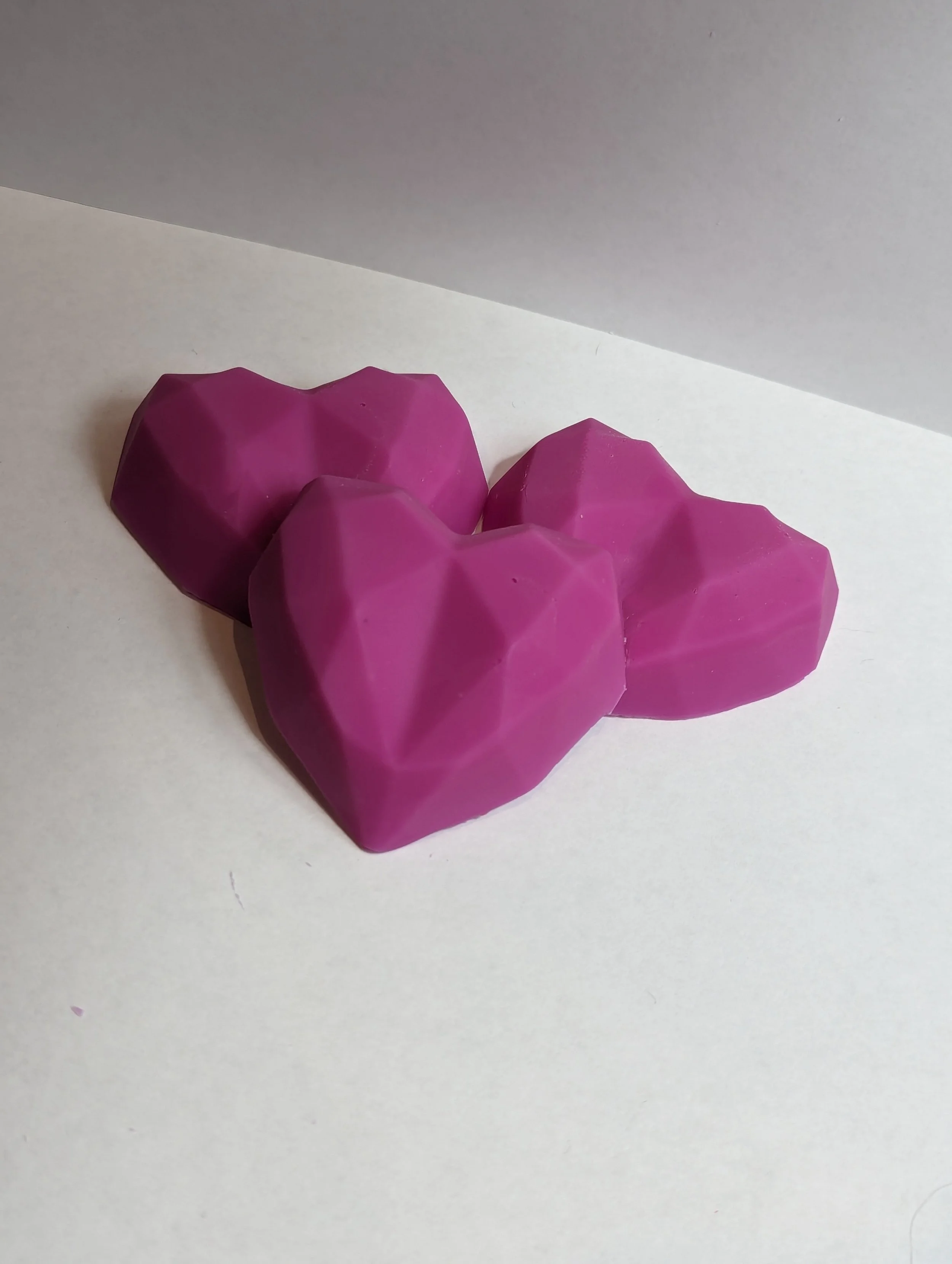 Three purple heart-shaped chocolates with geometric facets on a white surface.