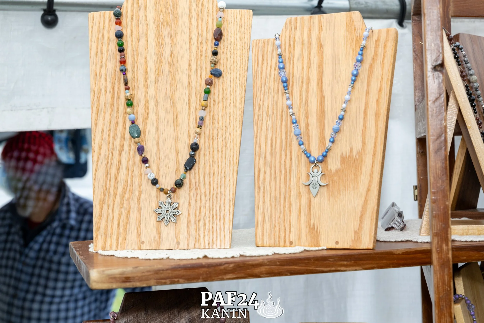 Colorful beaded necklaces displayed on wooden stands at a craft fair.