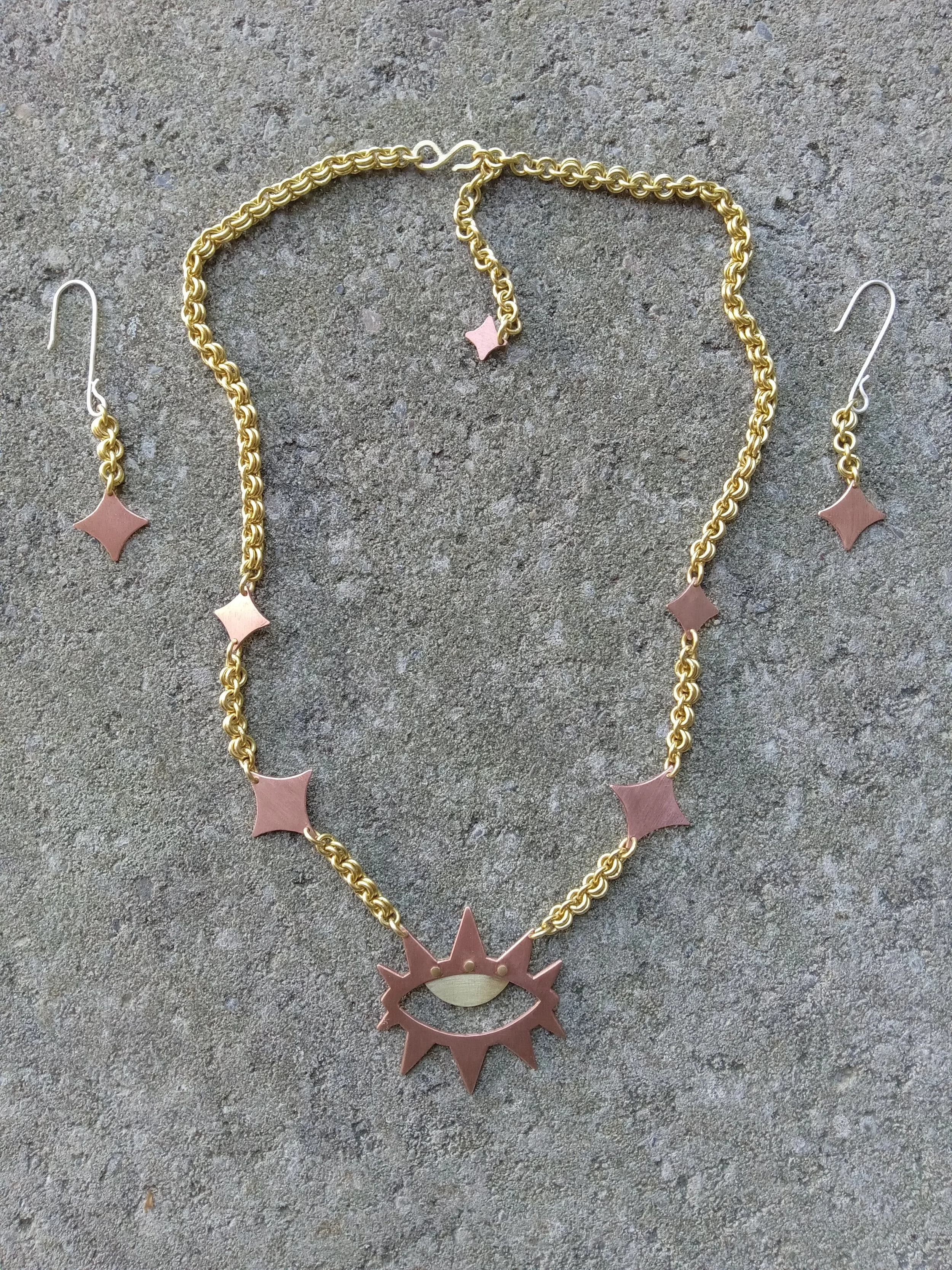 Gold necklace and earrings with pink star-shaped and sun-shaped pendants on a gray textured background.