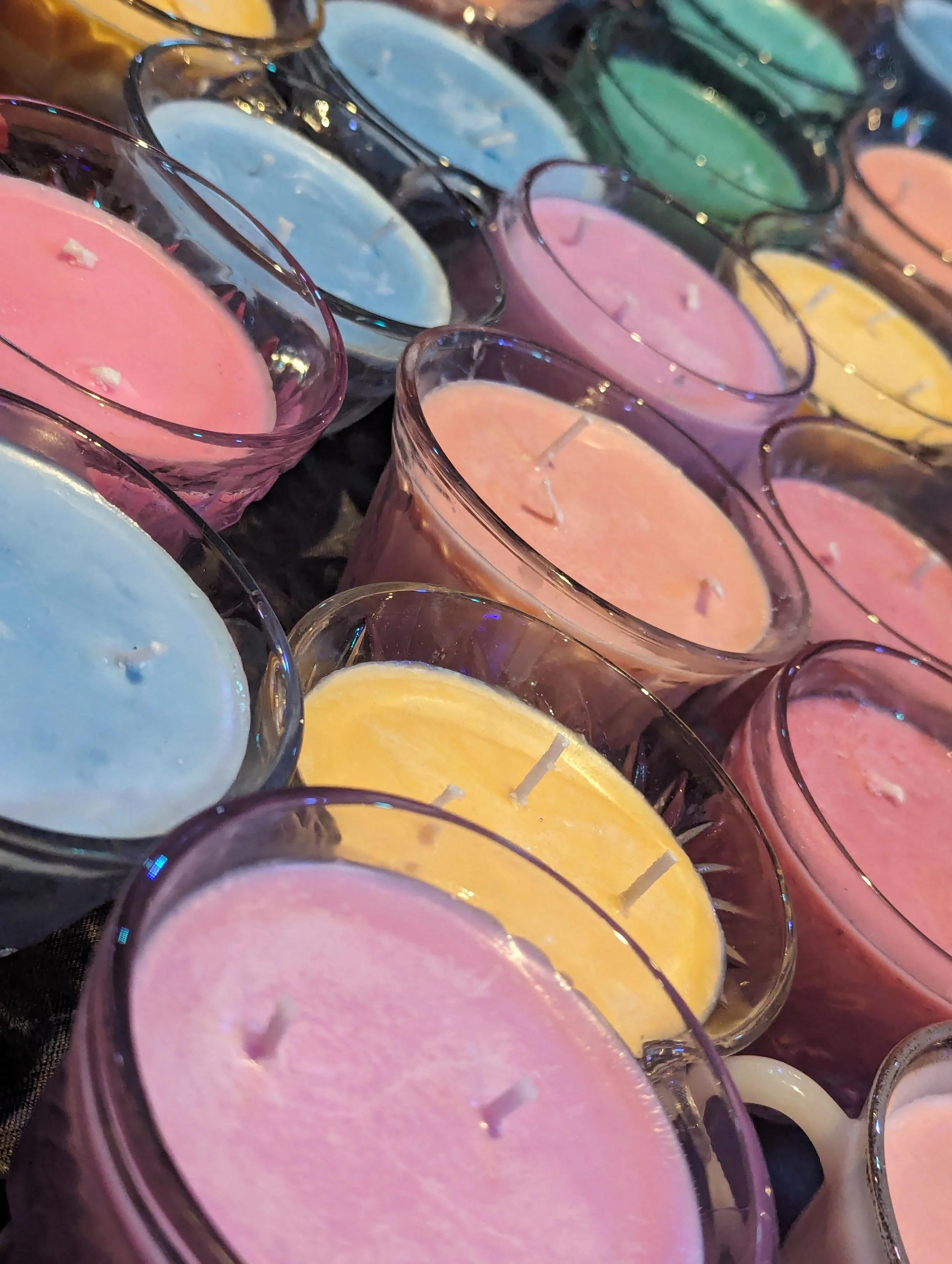A collection of colorful candles in glass holders, including pink, blue, yellow, green, and orange.