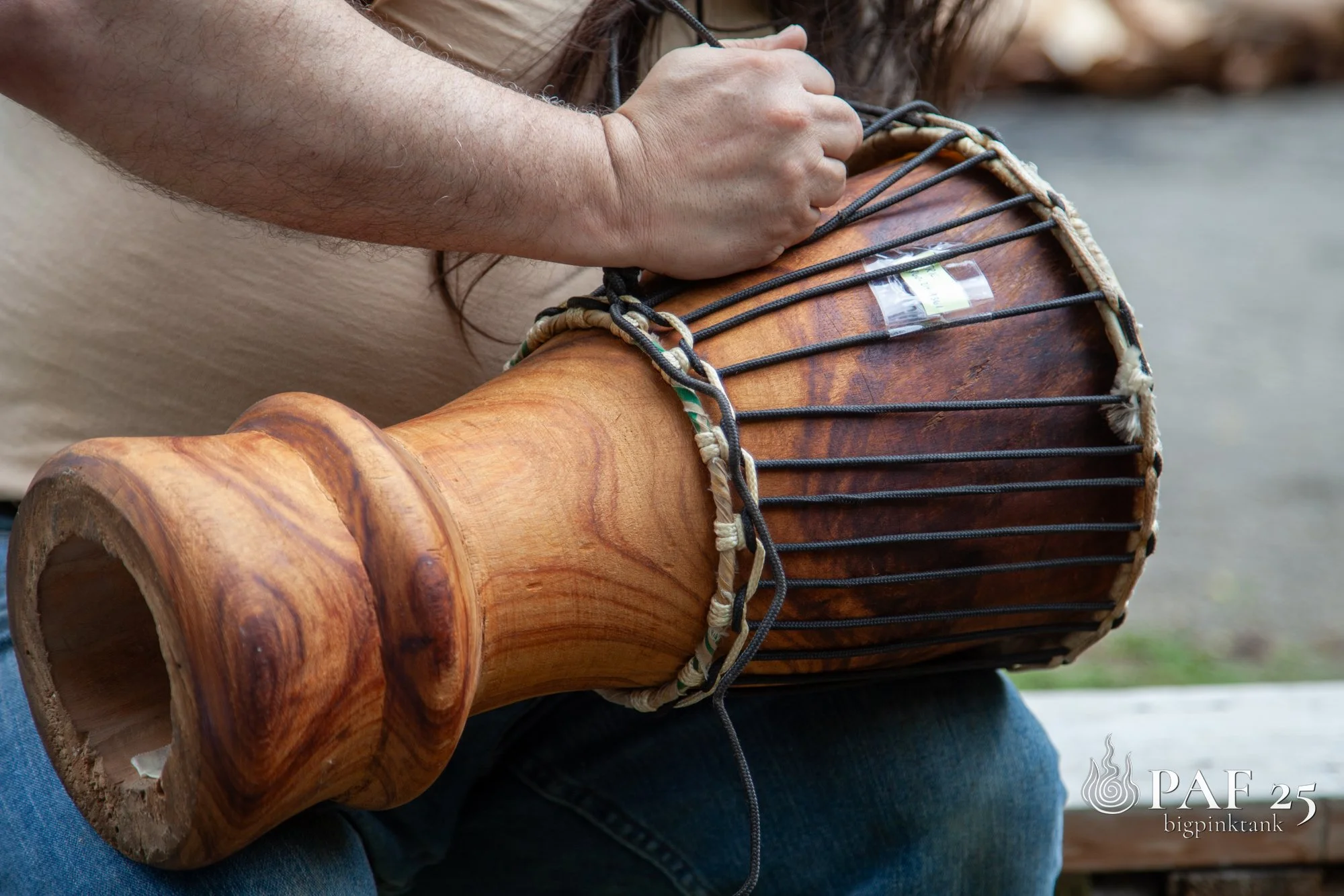 Close-up of a person adjusting a wooden drum, sitting outdoors, with natural background.