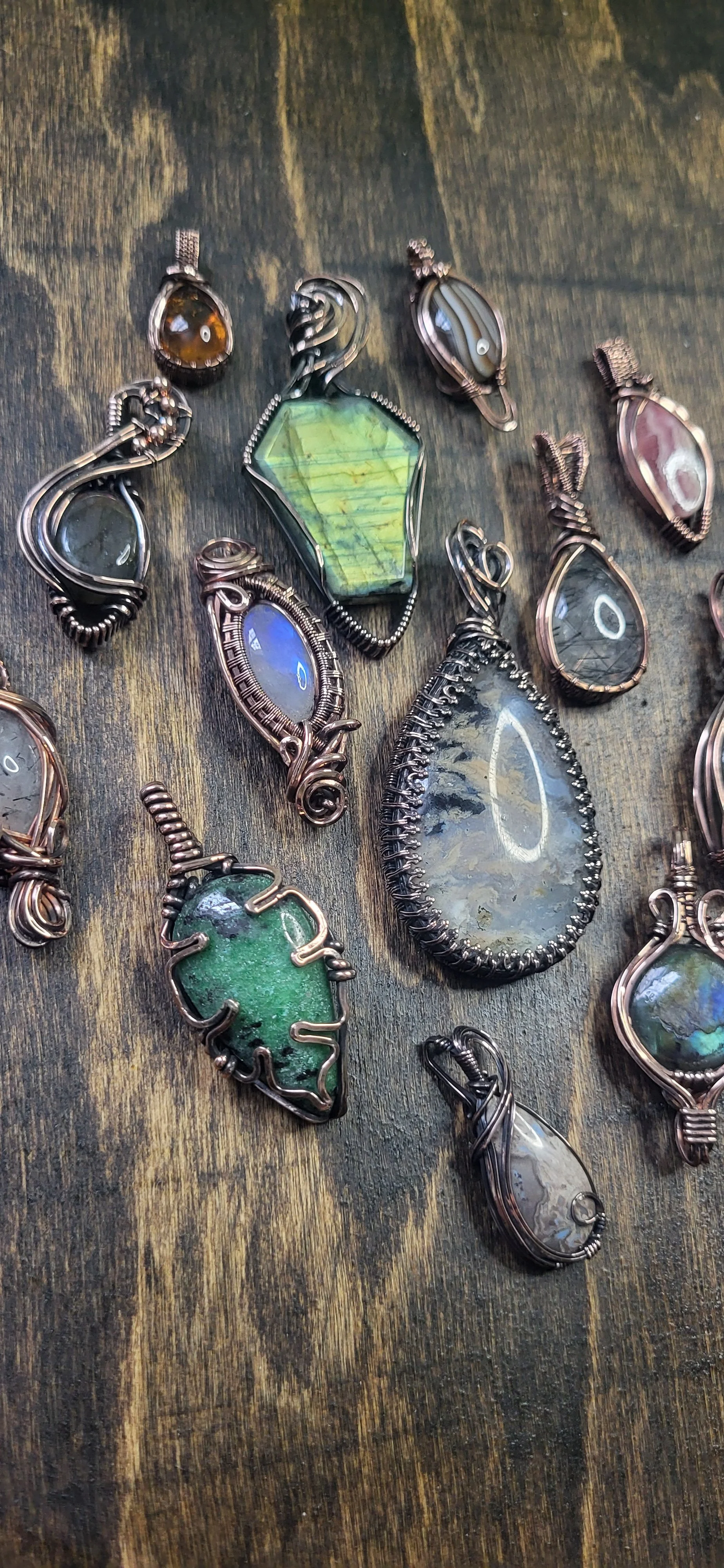 Assorted gemstone pendants with wire wrapping on a wooden surface.