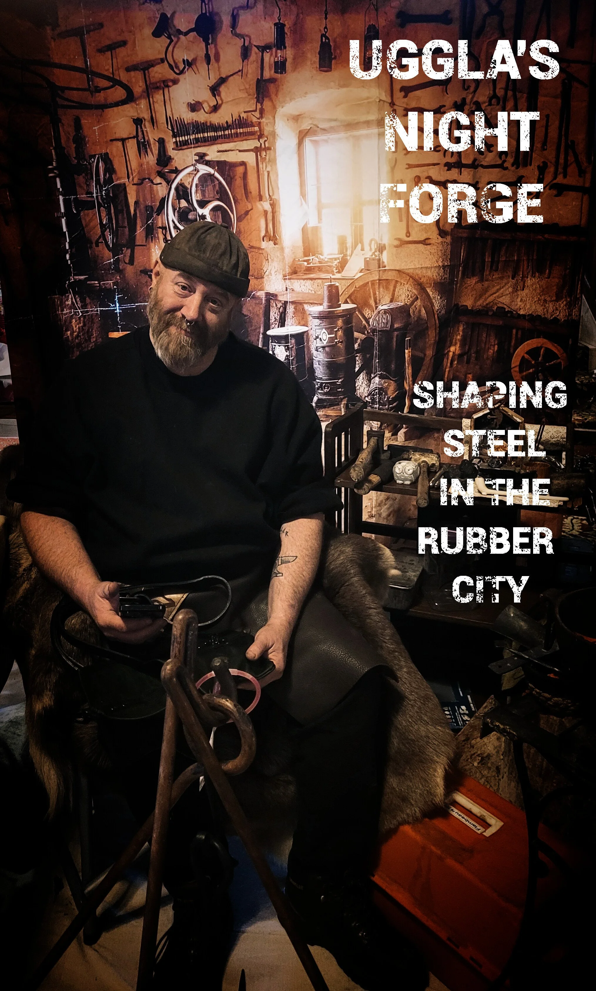 A bearded man wearing a black shirt and cap sitting on a chair in front of a workshop-themed backdrop with tools hanging on the wall. There is text on the image that says 'Ugglas Night Forge' and 'Shaping Steel in the Rubber City'.