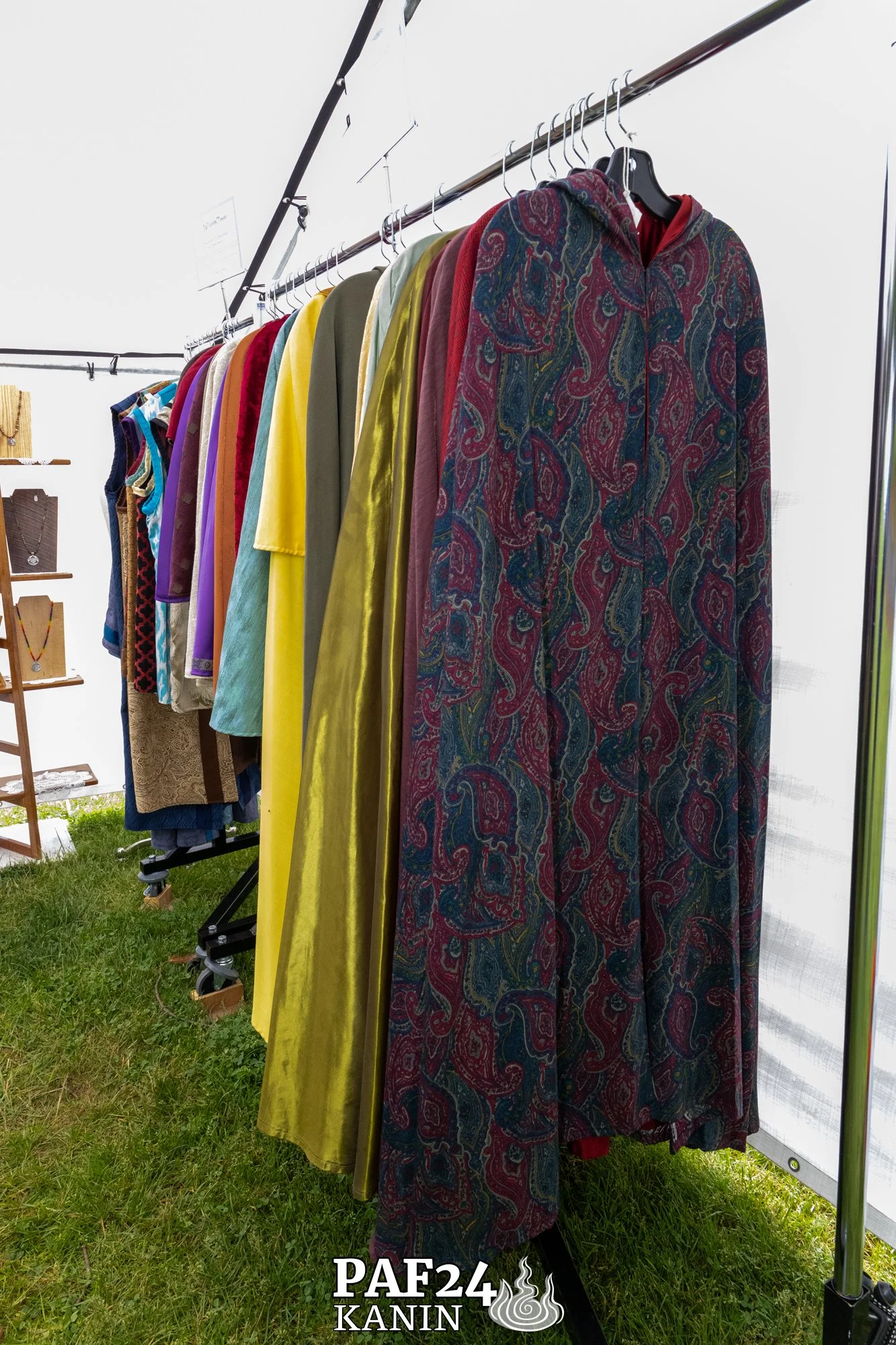 A rack of colorful jackets and dresses hanging on a clothing rack in an outdoor setting, with grass visible underneath.