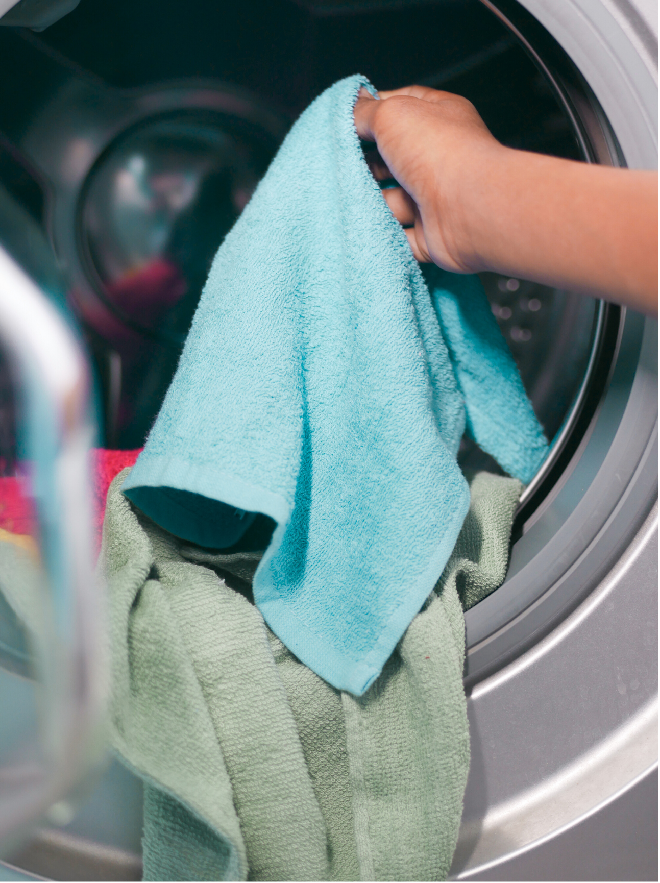 A person's hand loading a blue towel into a washing machine, in Davis California, at Davis Laundry clean laundromat