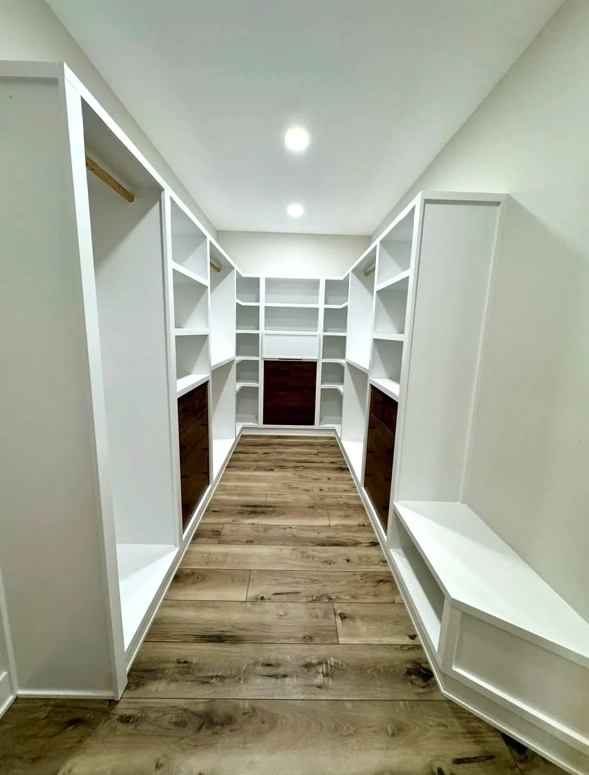 Custom walk-in closet with built-in white shelving, hanging rods, wood drawer storage, open shelving, a built-in bench, recessed lighting, and wood-look flooring.