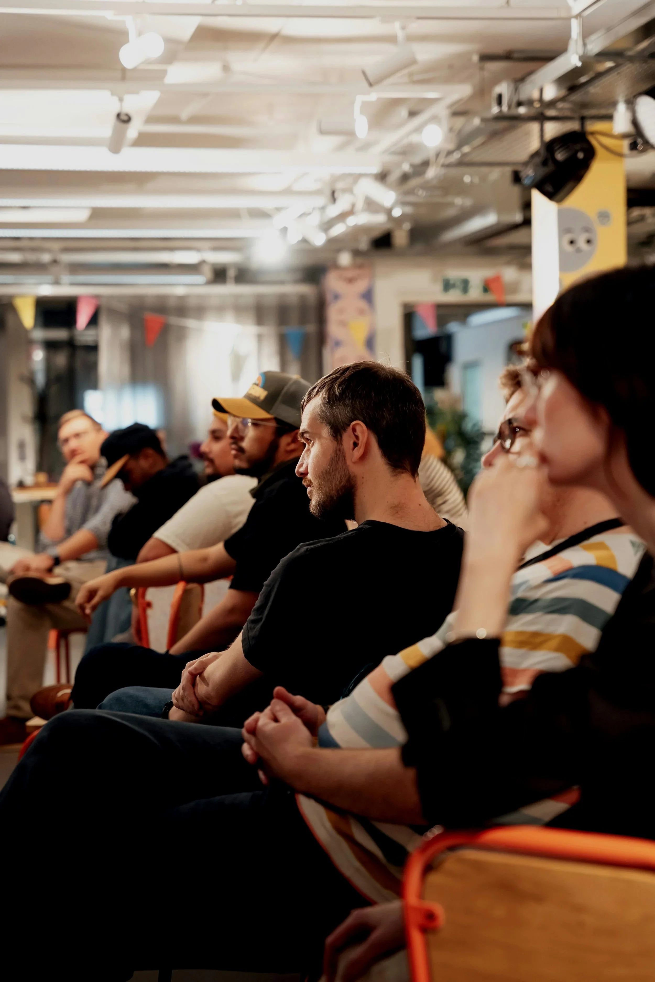 People sitting in a row at an indoor event or presentation, attentively listening.