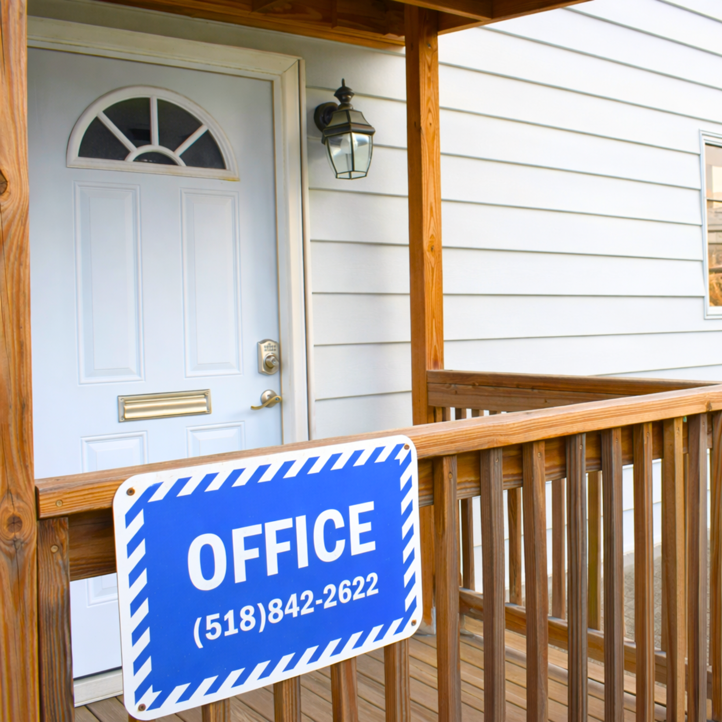 Front porch of a house with a white door, outdoor light fixture, and a blue sign that reads 'OFFICE' with a phone number.