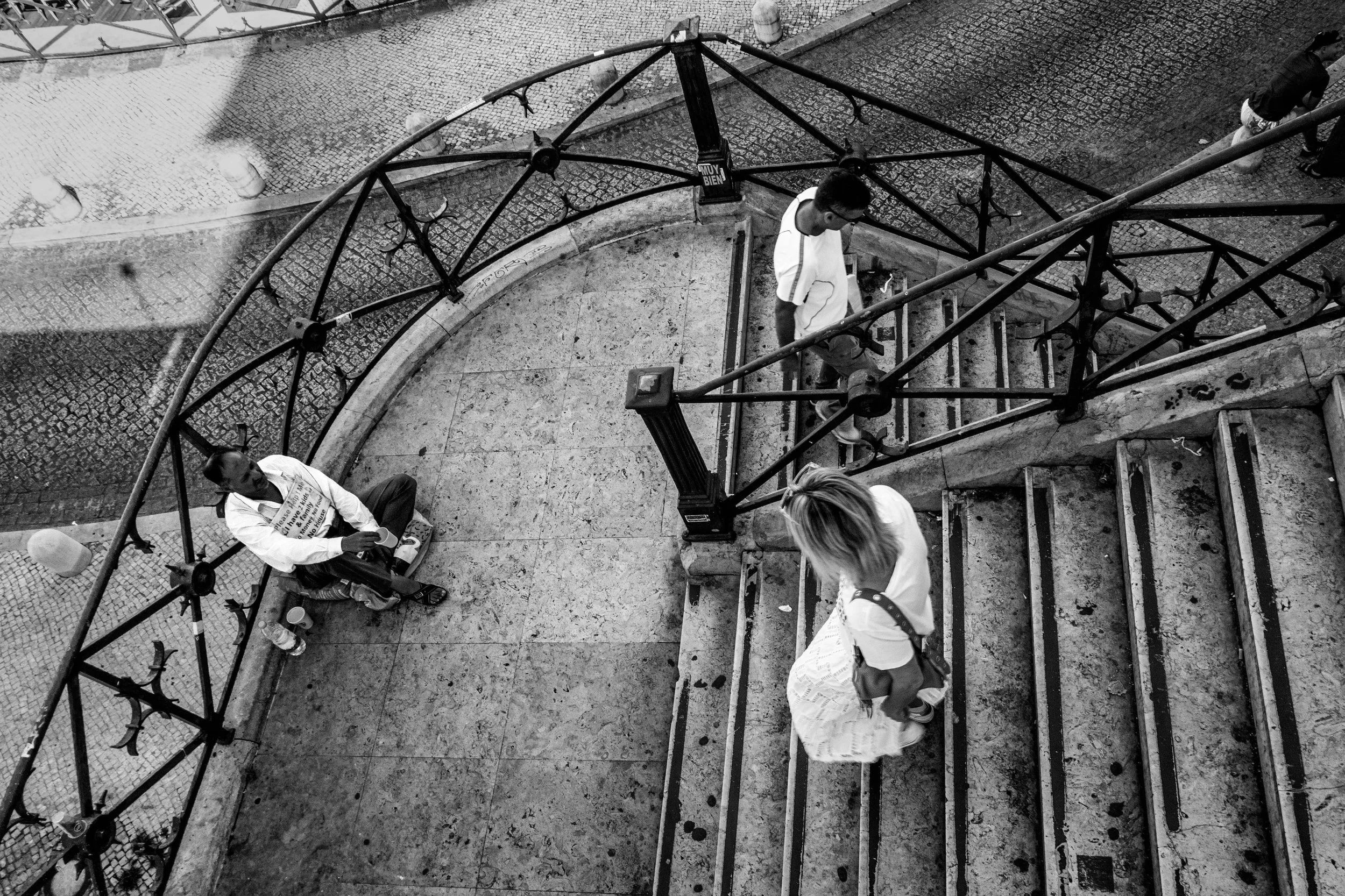 Imagem em preto e branco de uma escada de ferro com pessoas na rua vista de cima, incluindo um homem sentado e duas mulheres descendo a escada.