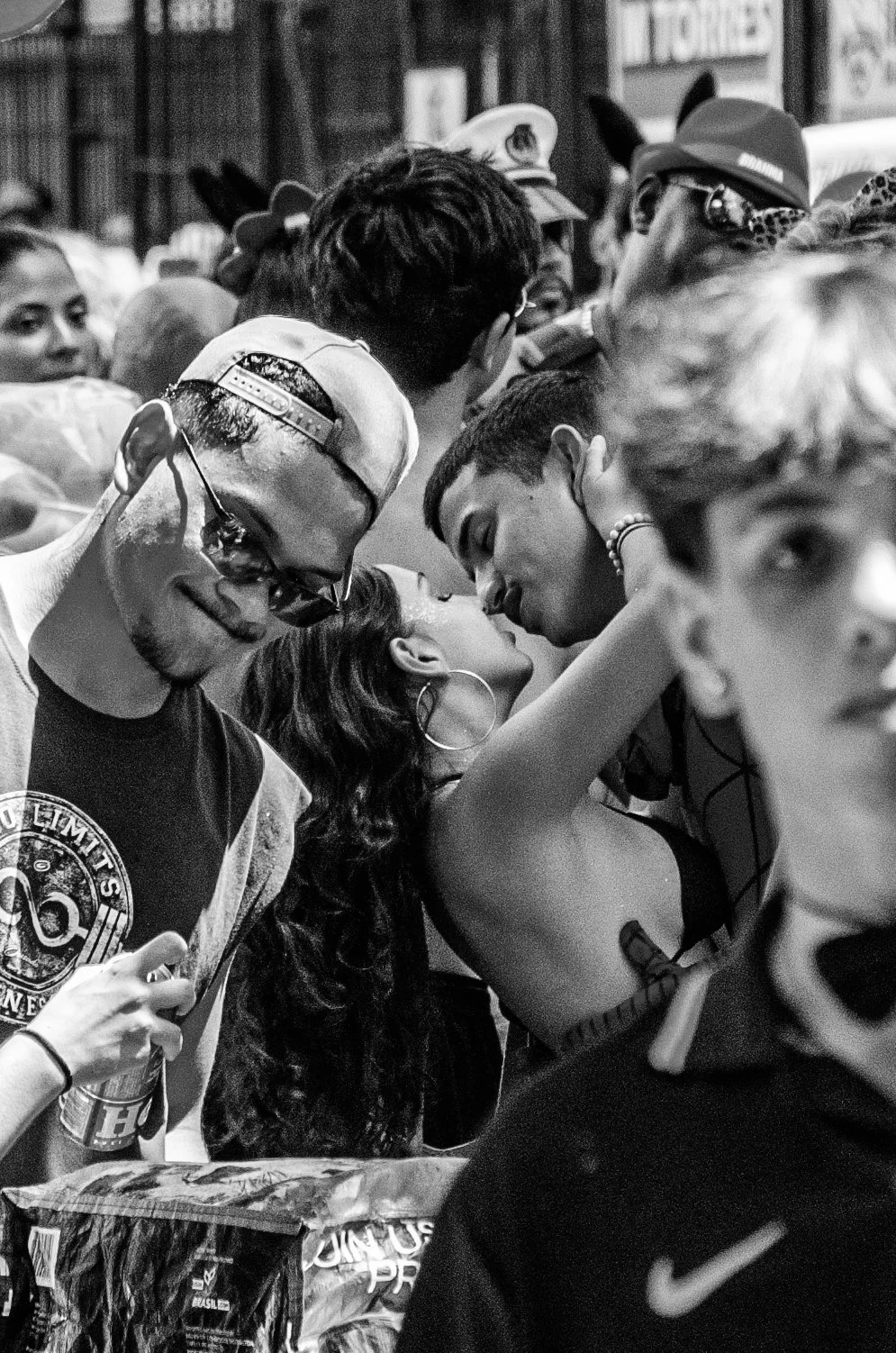 Grupo de jovens em uma fila, com alguns deles se beijando, em um ambiente fechado, possivelmente uma loja de conveniência ou livraria, em preto e branco.