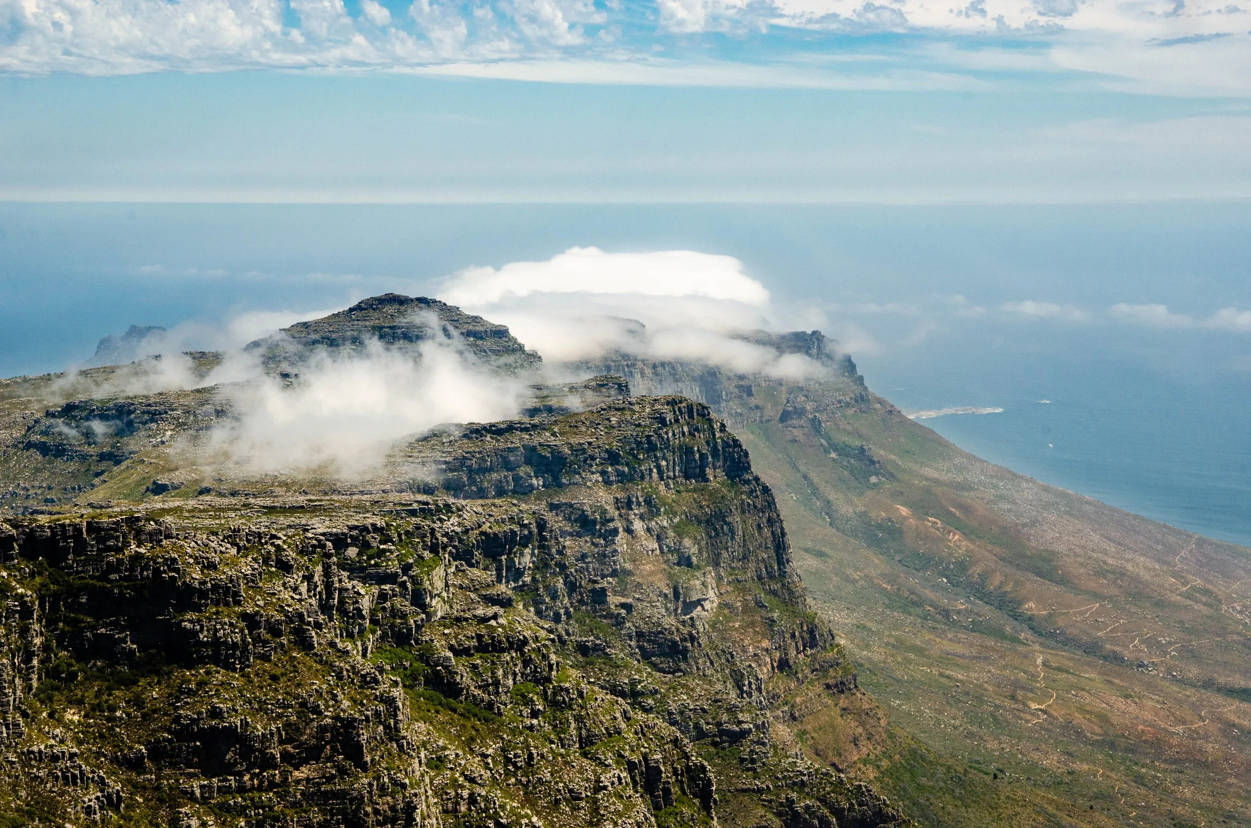Montanhas com formações rochosas, nuvens ao redor dos picos e vista do oceano ao fundo.