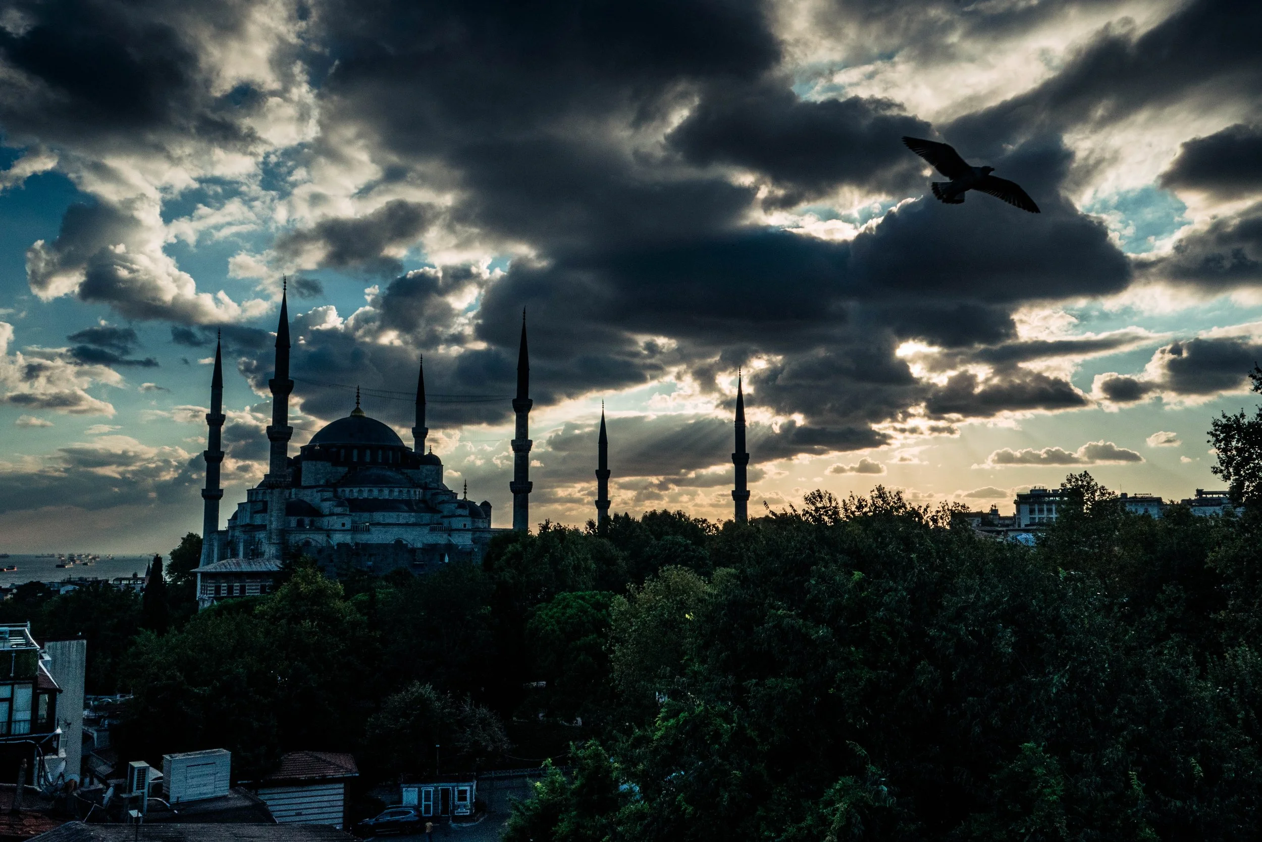 Vista da mesquita com várias torres durante o pôr do sol, céu com nuvens escuras e um pássaro voando no céu.