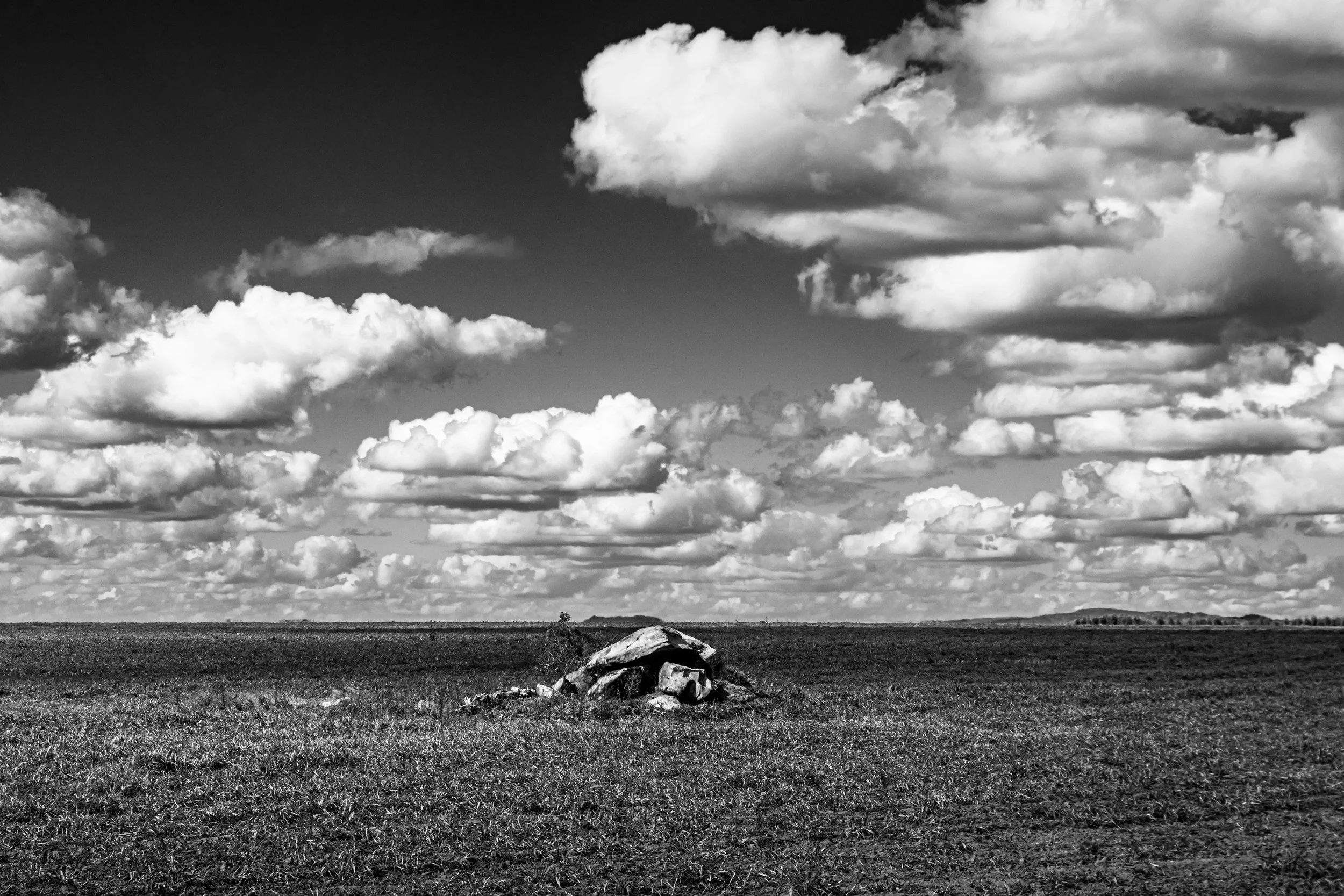 Campo aberto com uma formação rochosa no centro e céu com nuvens.