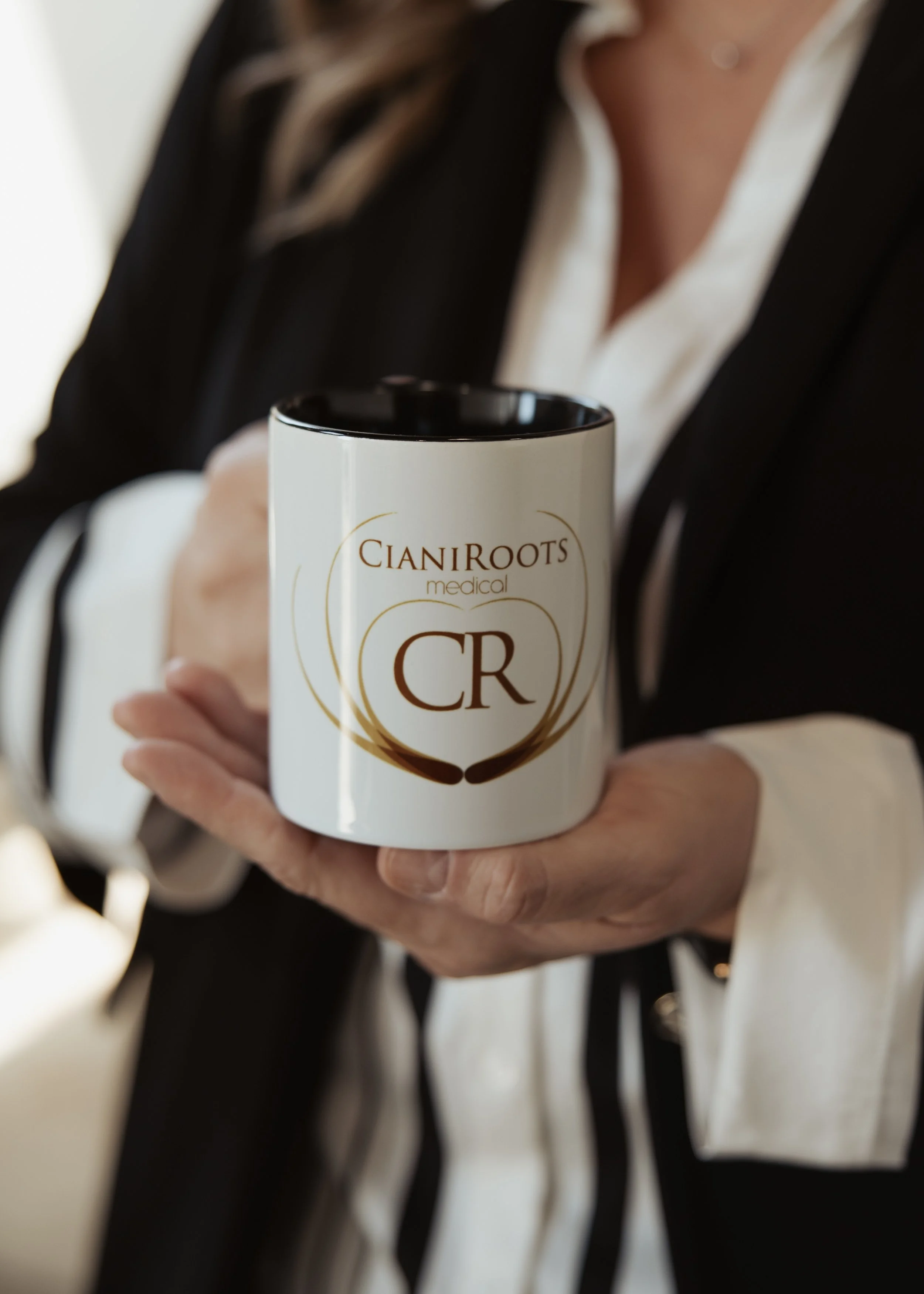 Person holding a white mug with the words 'Cian Roots Medical' and a logo printed on it.