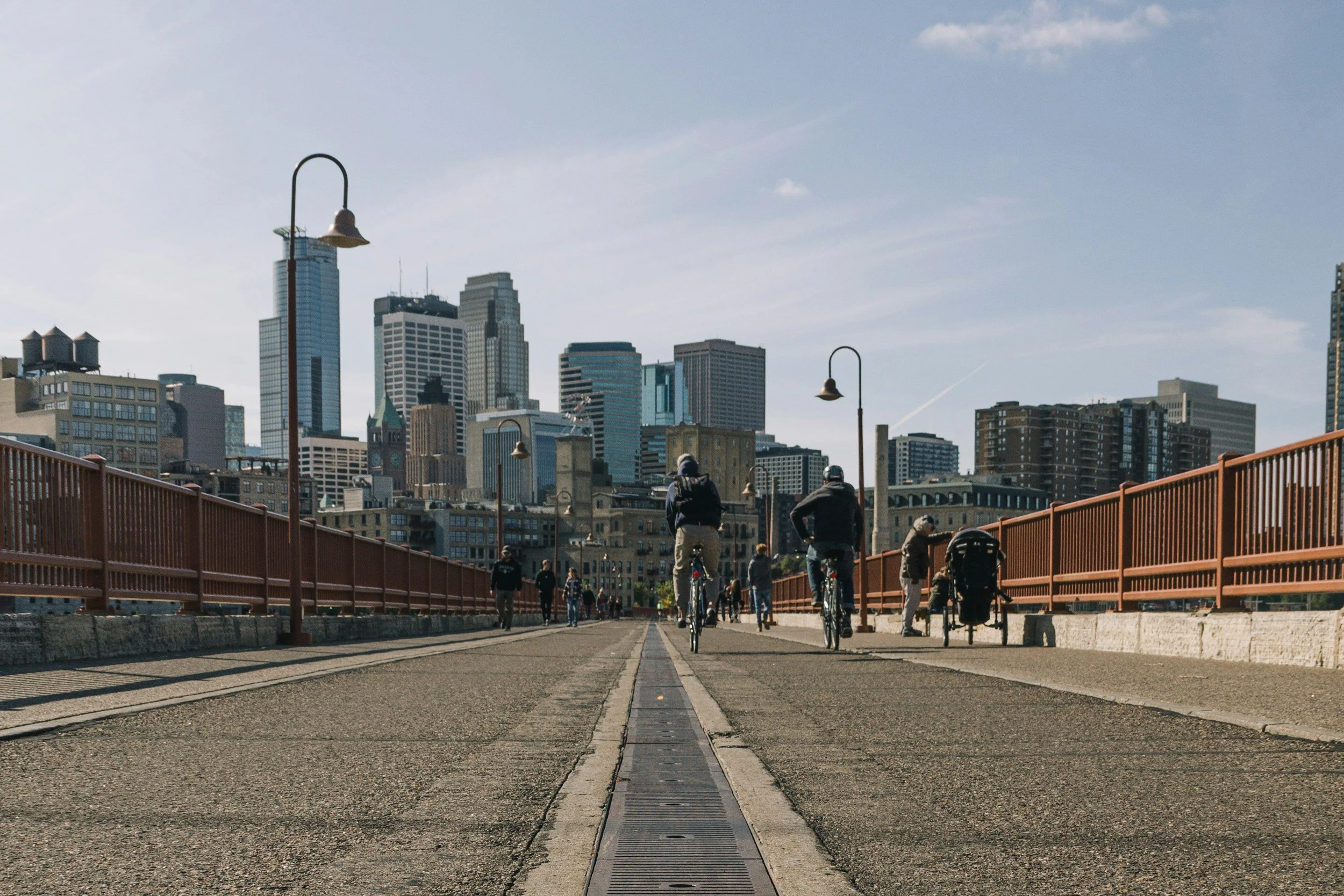People biking on a bridge in front of a city skyline with tall modern buildings.