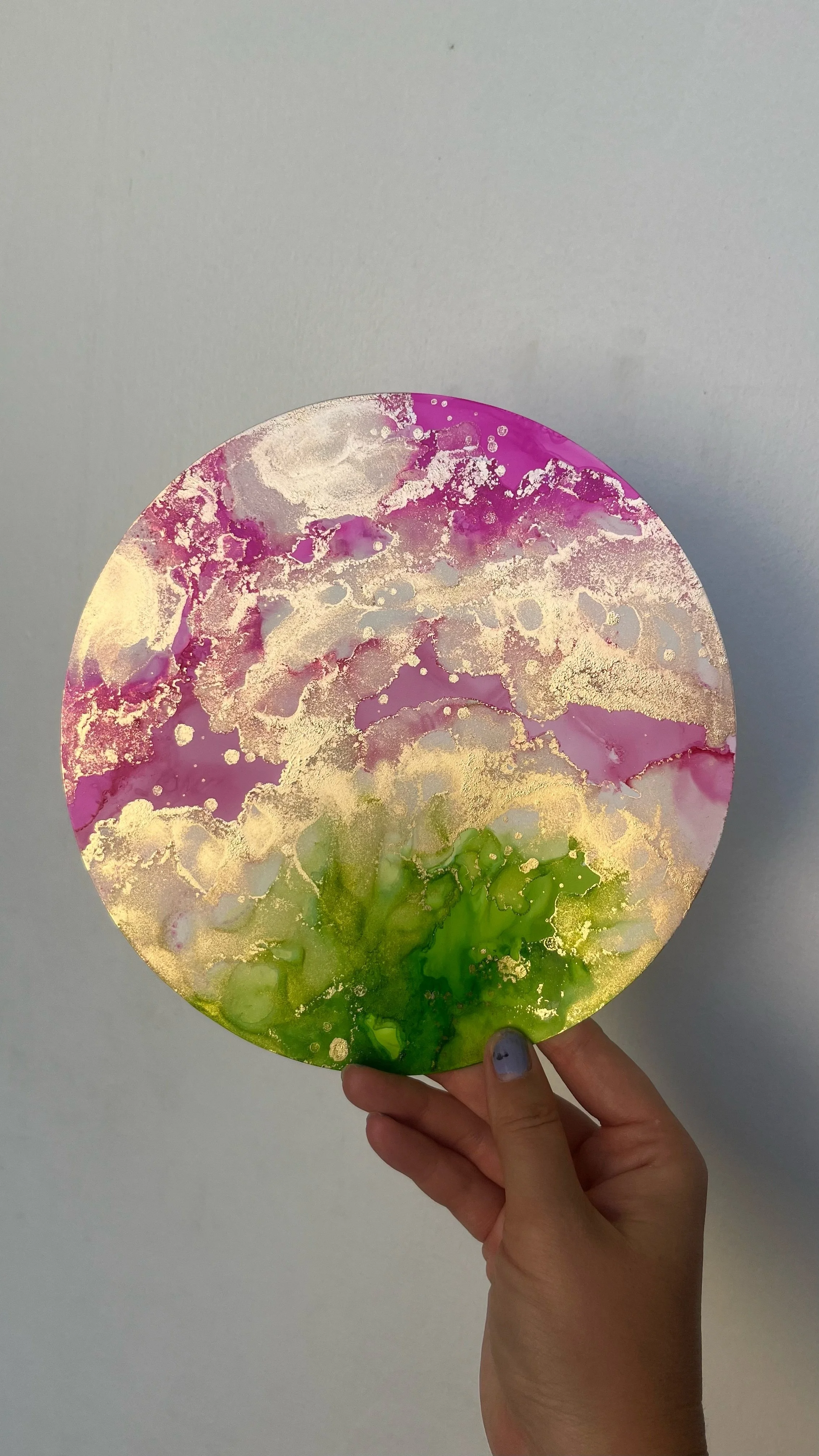 Hand holding a circular abstract painting with pink, green, and gold colors. This is an aura painting and it comes with an aura reading. An aura reader & aura artist made this.
